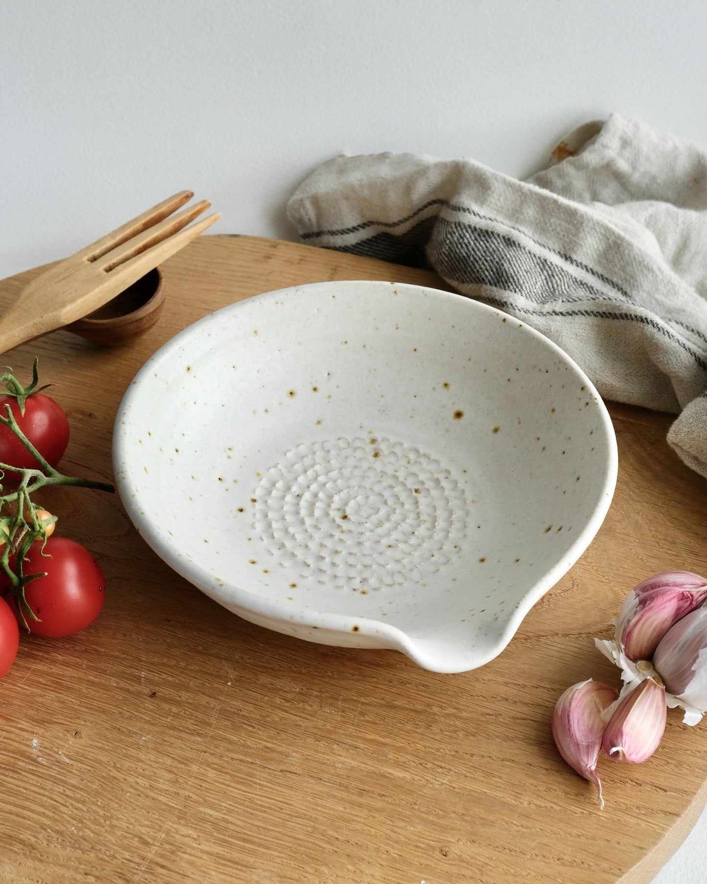 White ceramic grater bowl on a wooden surface with tomatoes and garlic