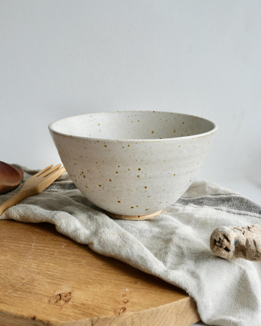 Ceramic bowl with speckled pattern on a wooden surface with a cloth and wooden utensils.