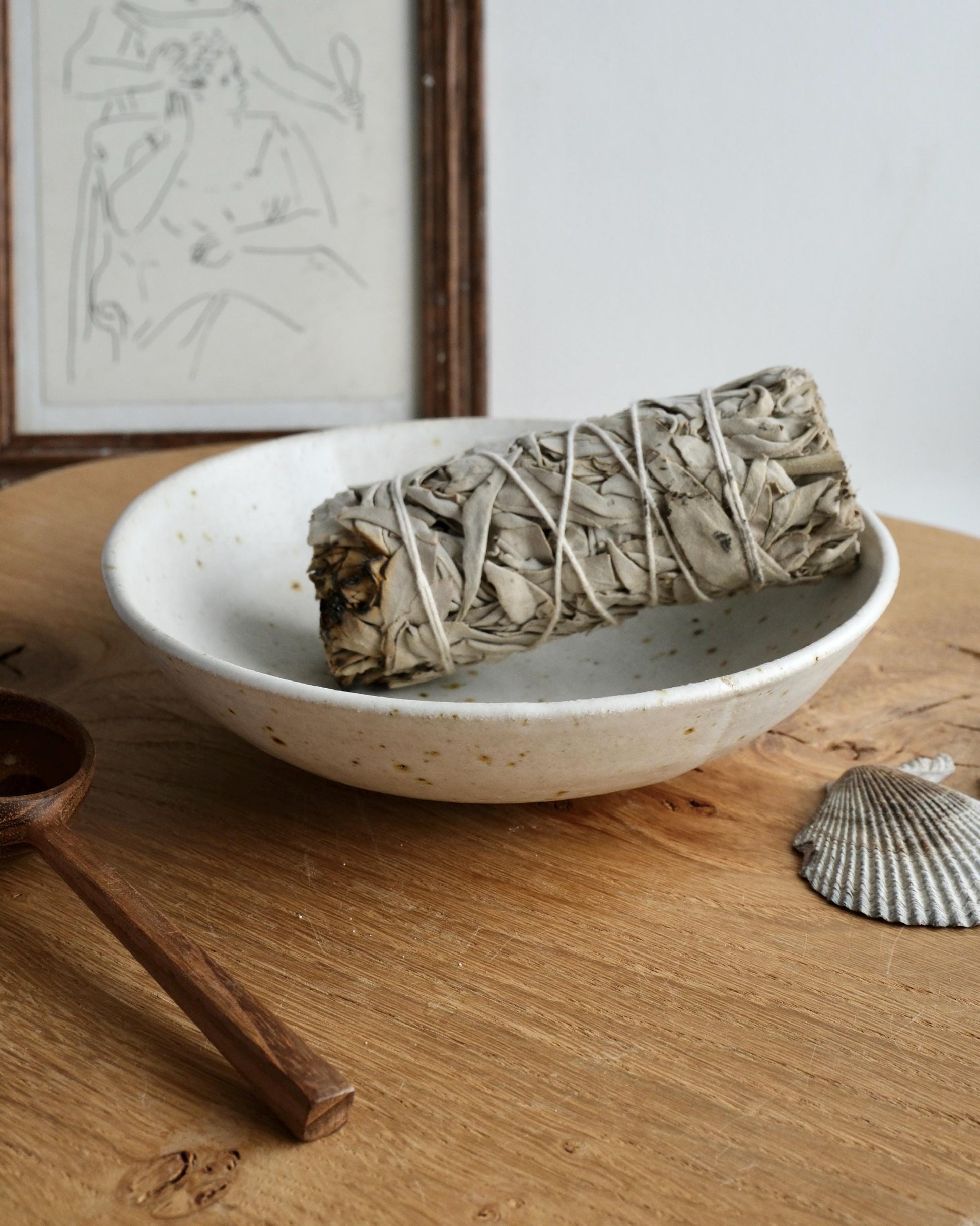 White ceramic bowl with a bundle of sage on a wooden surface