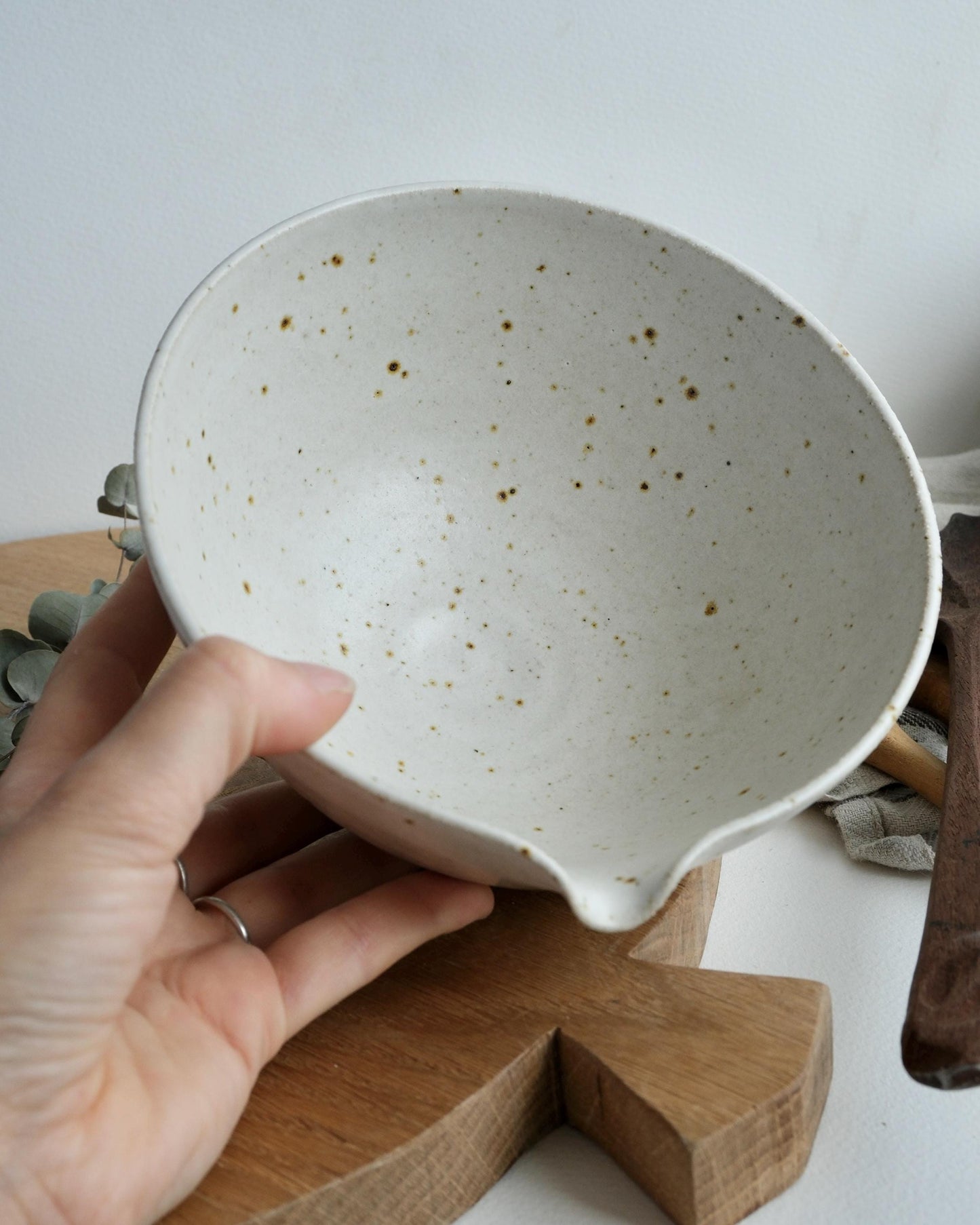 Hand holding a ceramic mixing bowl with a speckled pattern on a wooden stand.