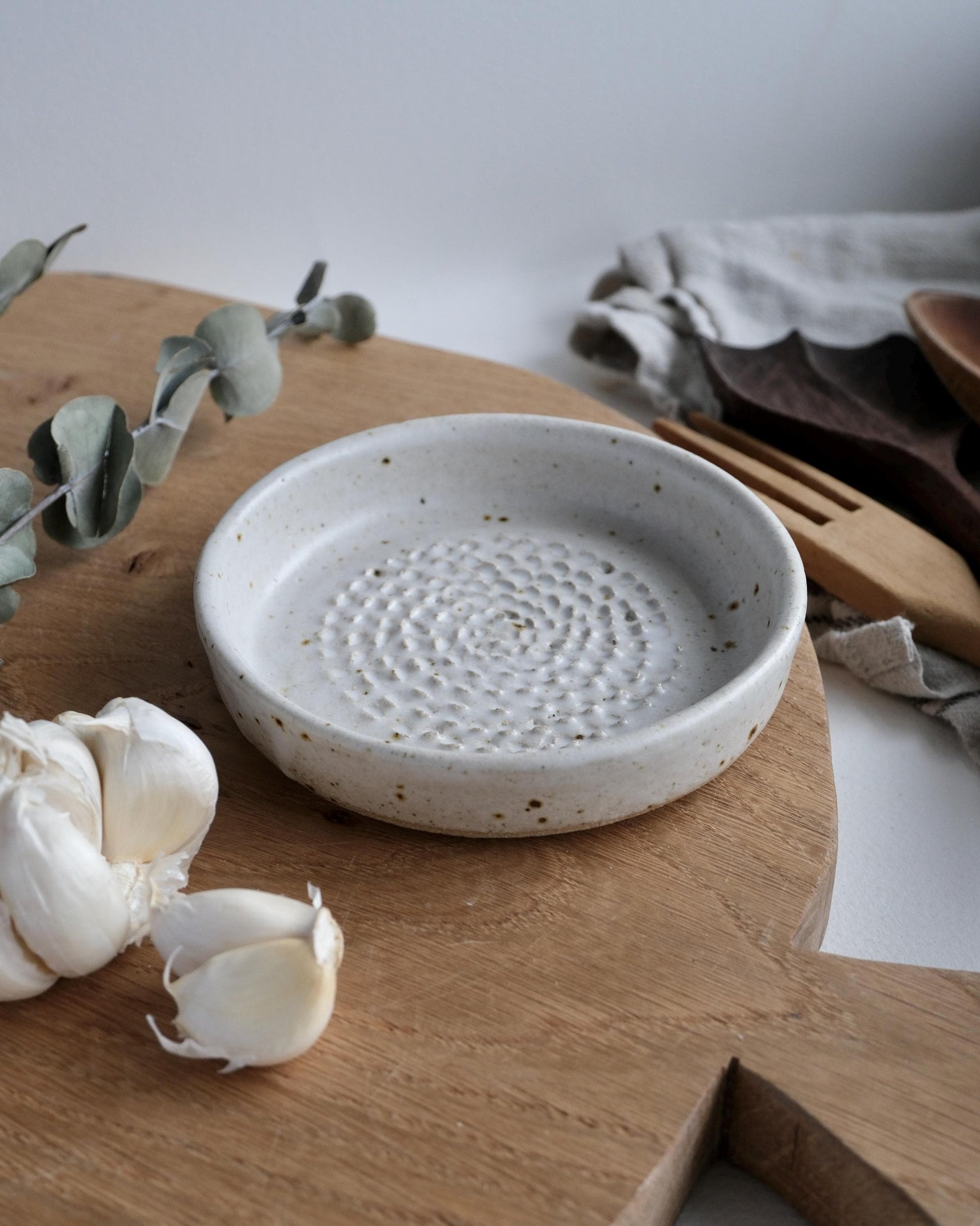 white Ceramic grater dish on a wooden surface with garlic and a wooden fork.
