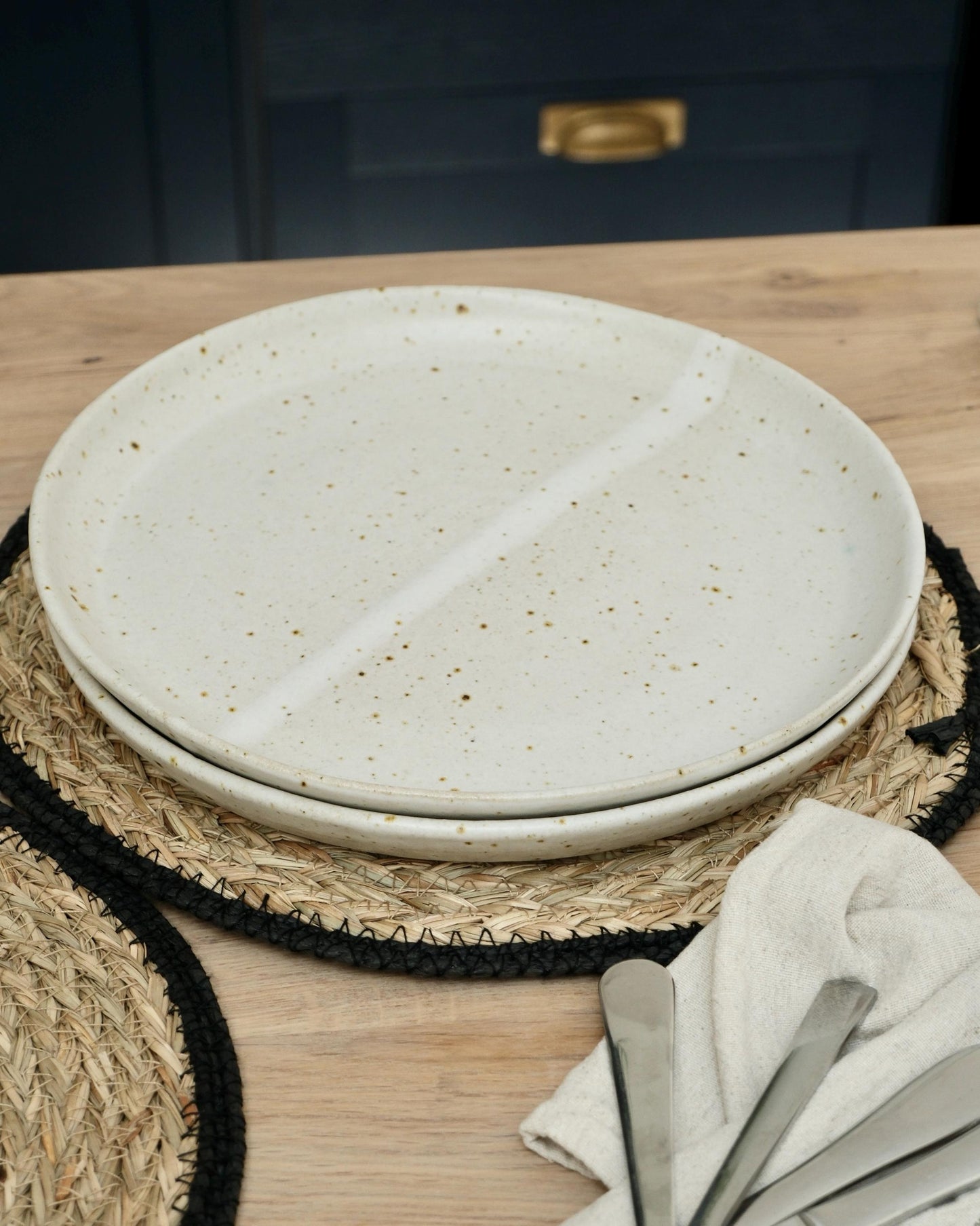 White ceramic plates on a woven placemat with cutlery on a wooden surface.