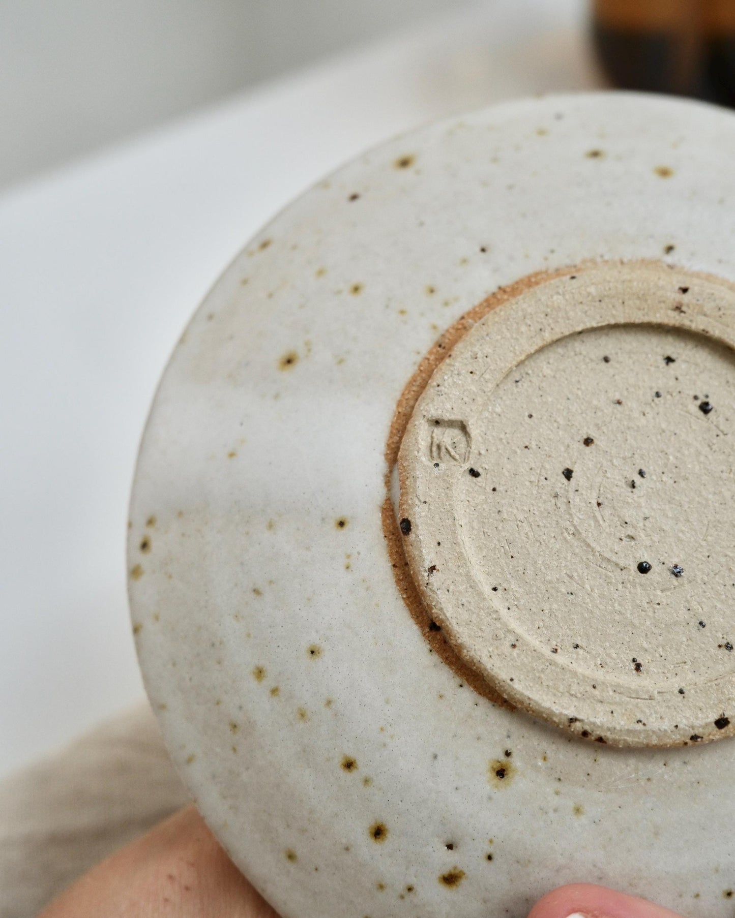 Close-up of the bottom of a white ceramic dish with speckled texture and a visible brand logo.