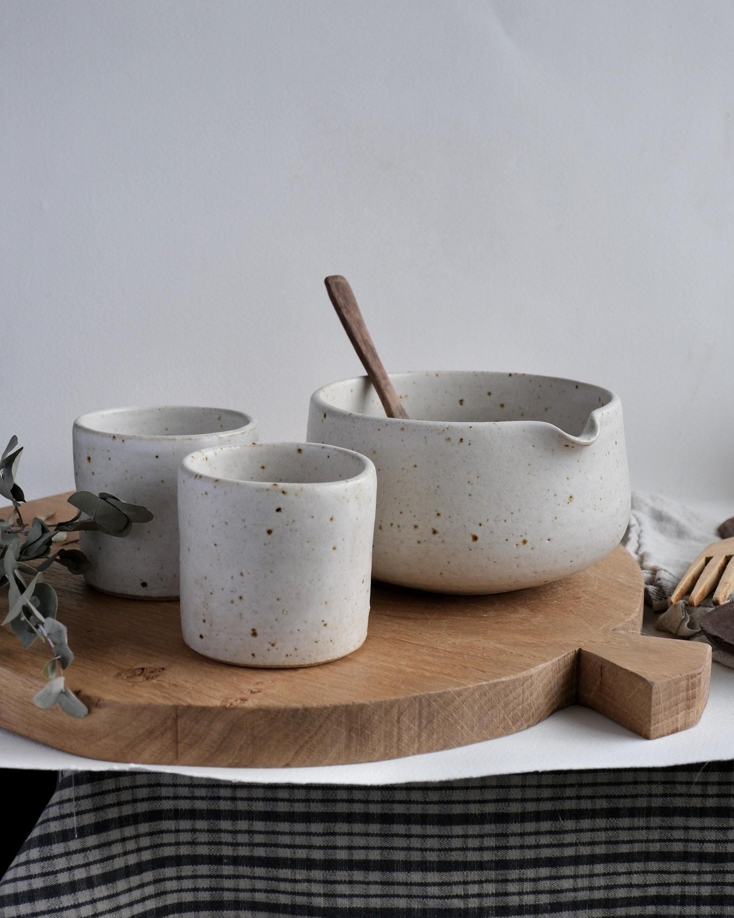 Set of white ceramic cups next to a matcha mixing bowl on a wooden board with a white background