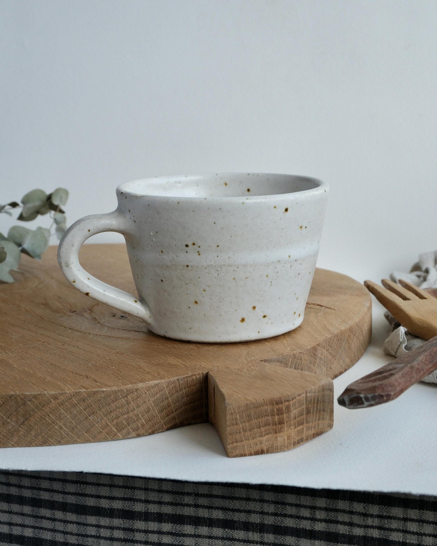 Speckled white ceramic coffee mug on a wooden cutting board with a neutral background