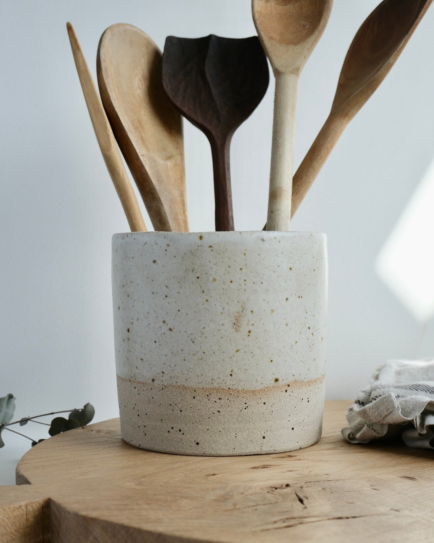 white ceramic utensil holder with wooden spoons in it on a wooden chopping board