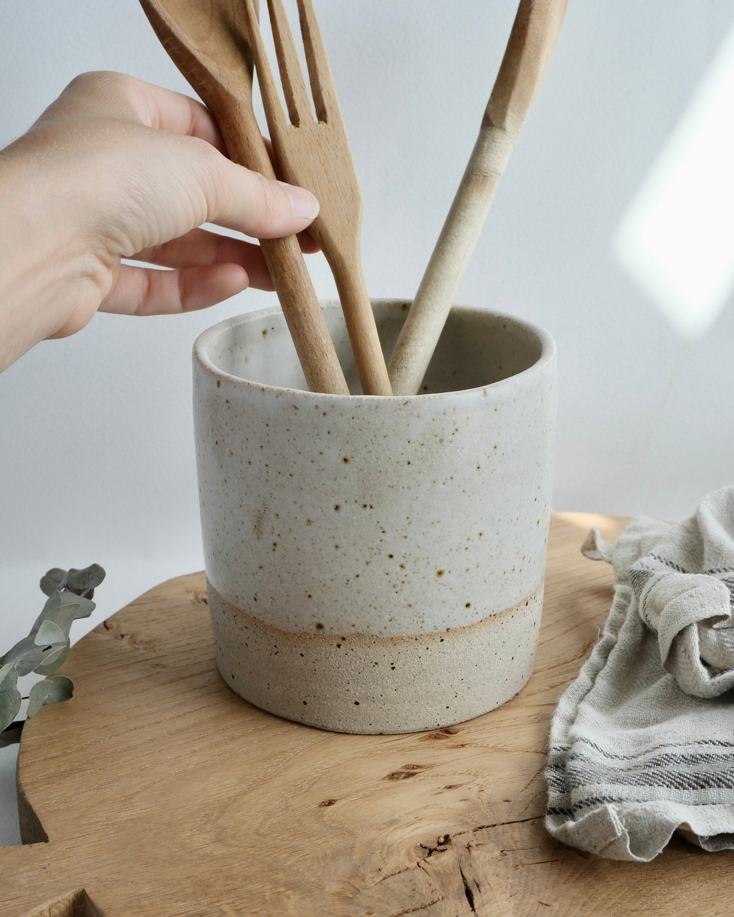 hand holding wooden spoons in a white ceramic utensil pot 