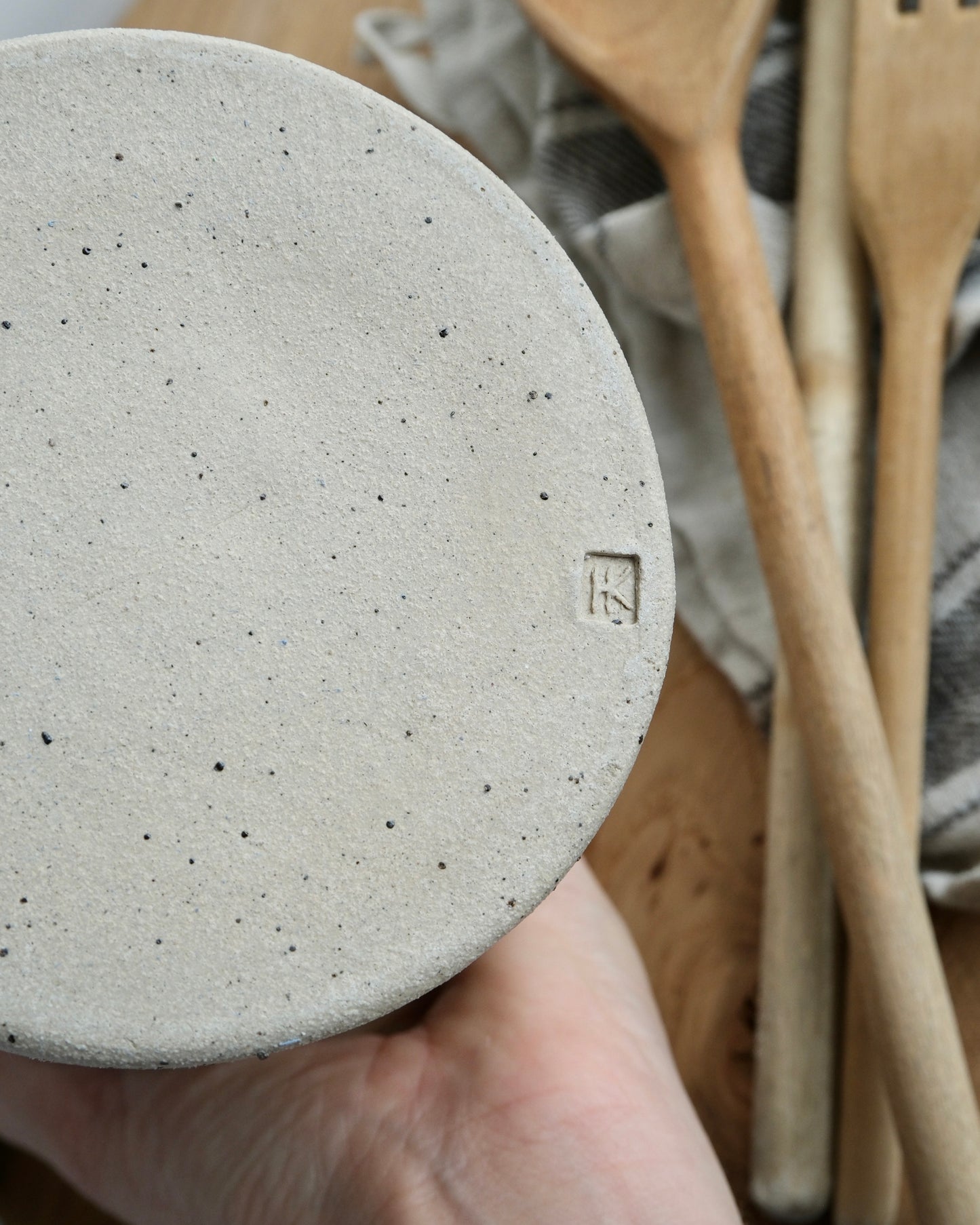 Close-up of a ceramic pot with a brand logo with wooden utensils in the background