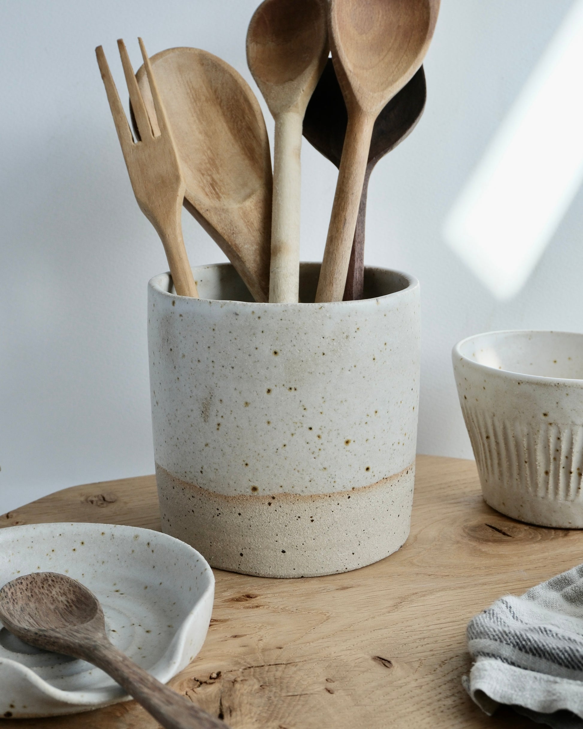 Set of wooden utensils in a ceramic holder on a wooden surface with a white background