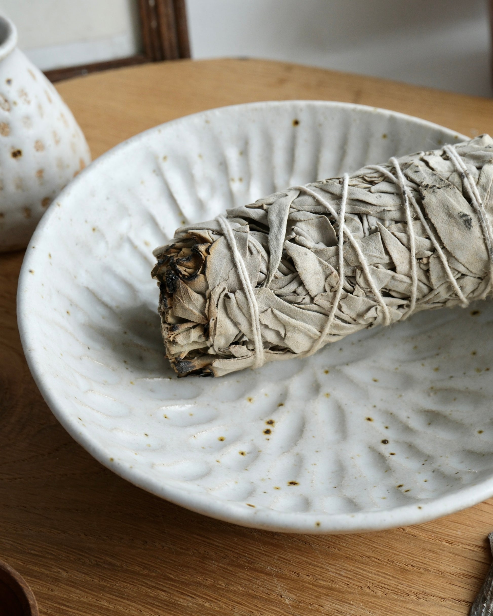 White sage smudge stick on a textured ceramic bowl with a blurred background