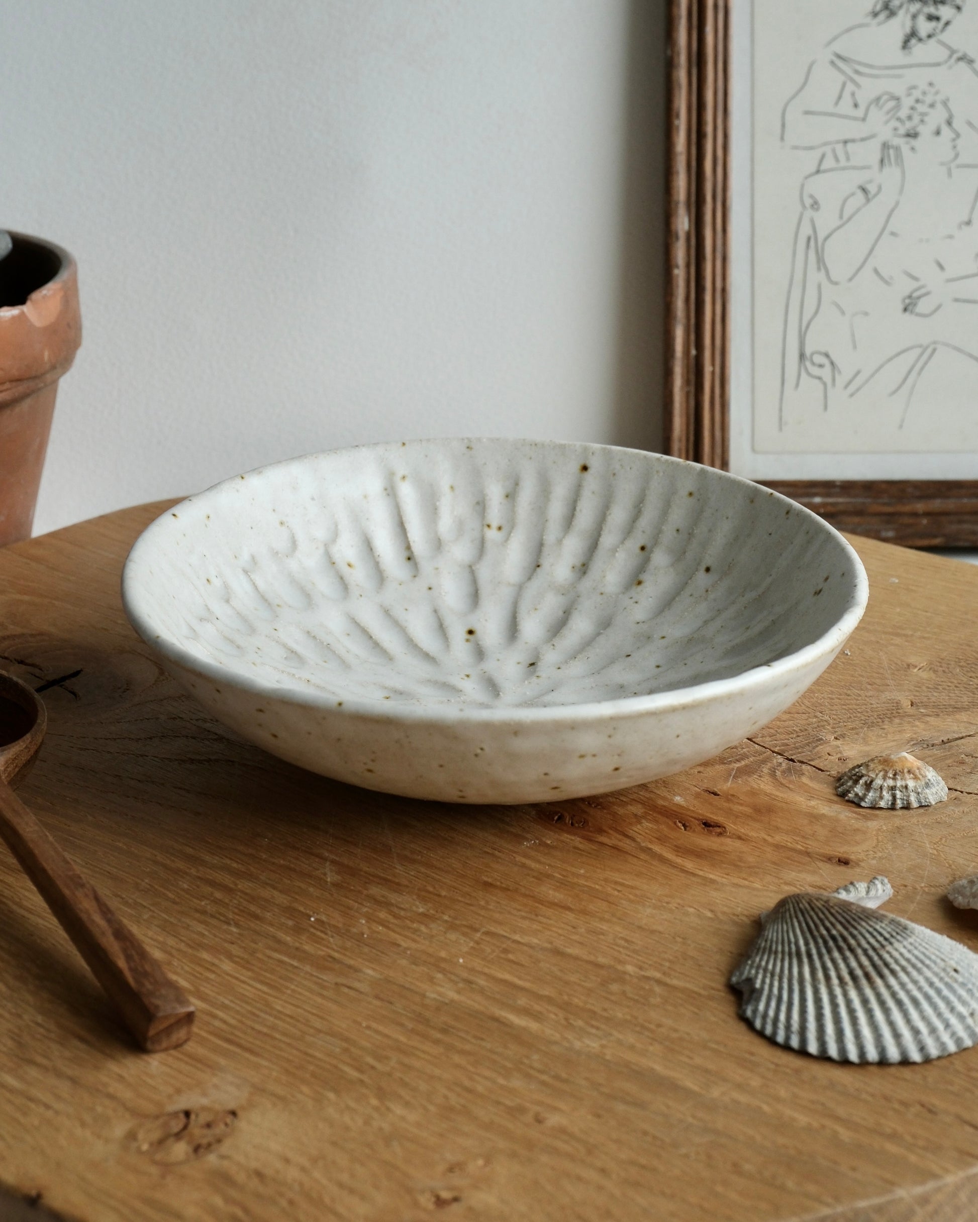 Handmade white ceramic dish bowl on a wooden surface with a framed picture in the background