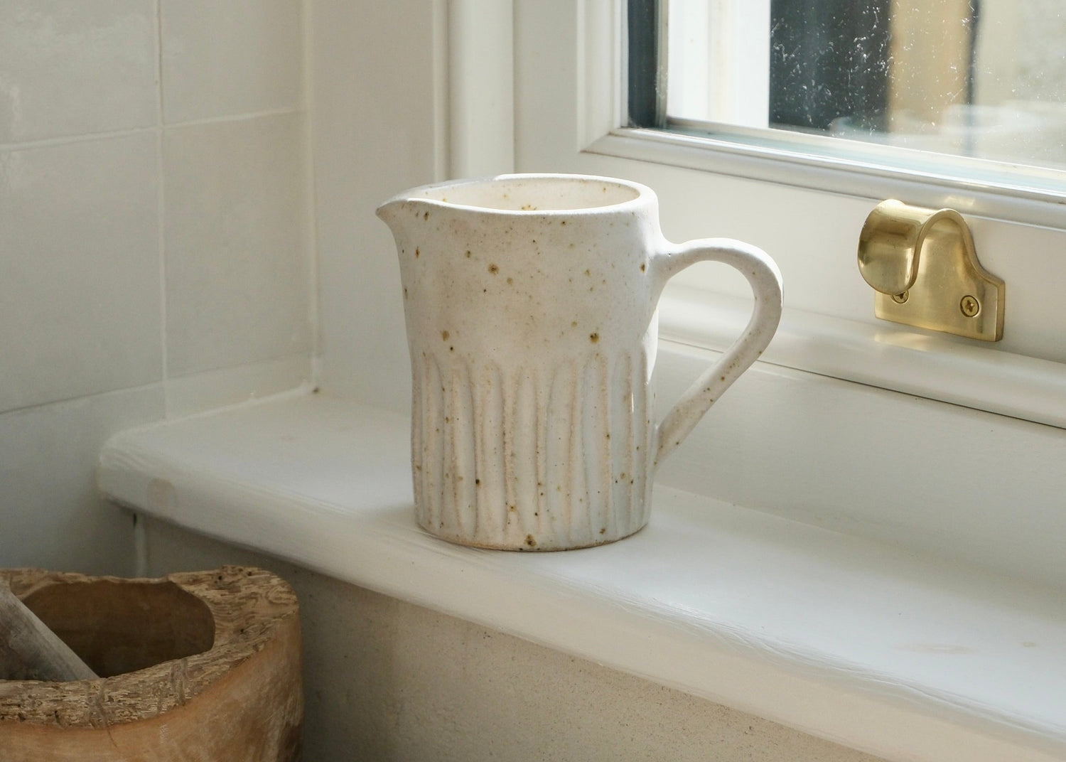 Ceramic pitcher on a windowsill with a textured wall and window in the background