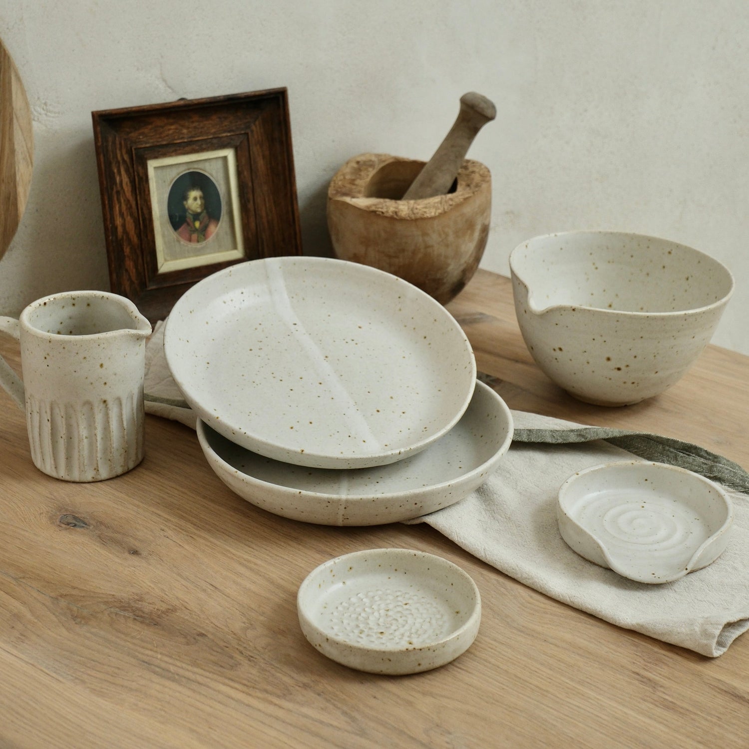 Set of white speckled handmade ceramic dishes and bowls on a wooden table with a neutral background