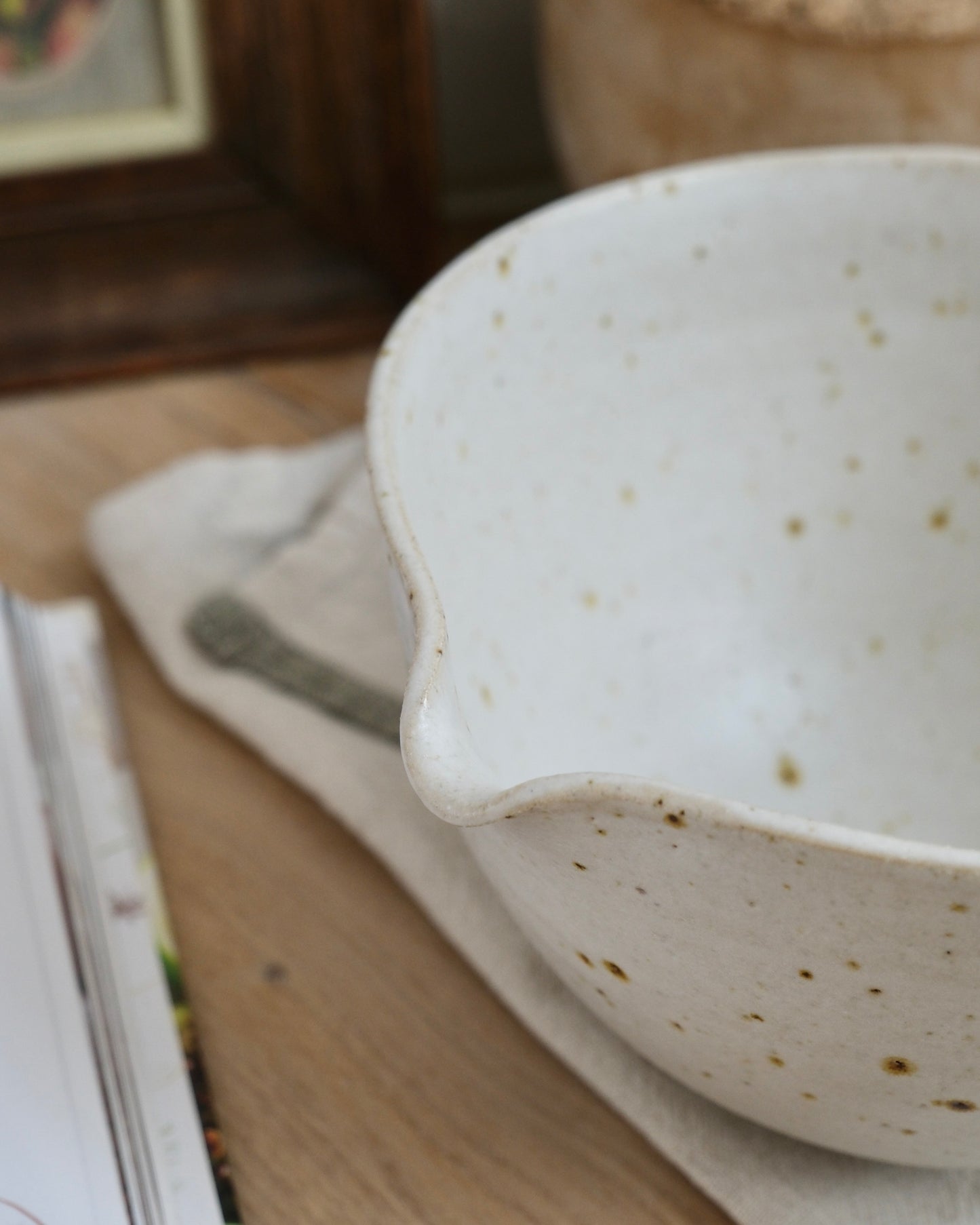 white Ceramic mixing bowl with a pouring spout and speckled texture on a wooden surface