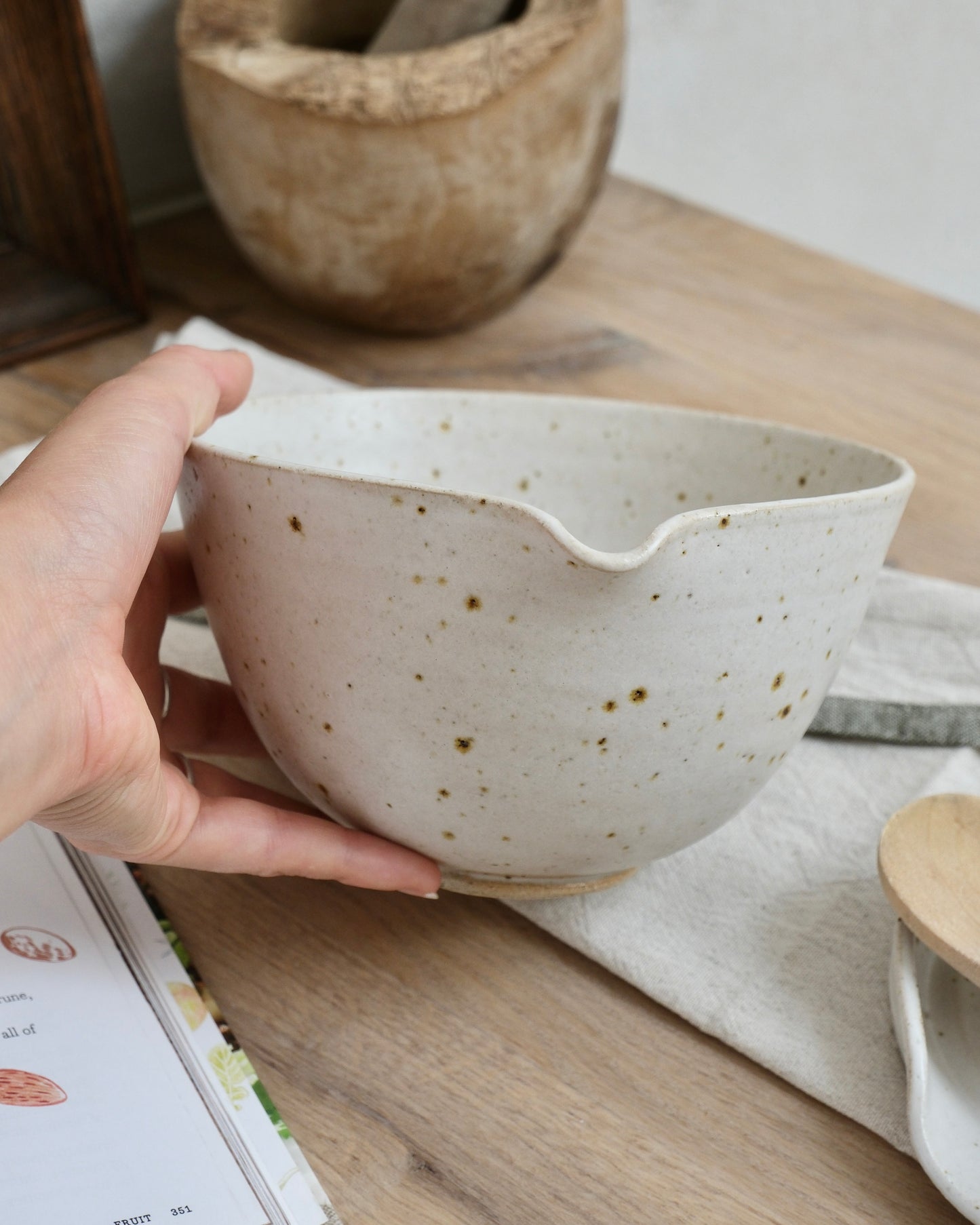 Hand holding a white ceramic mixing bowl with speckled pattern on a wooden surface