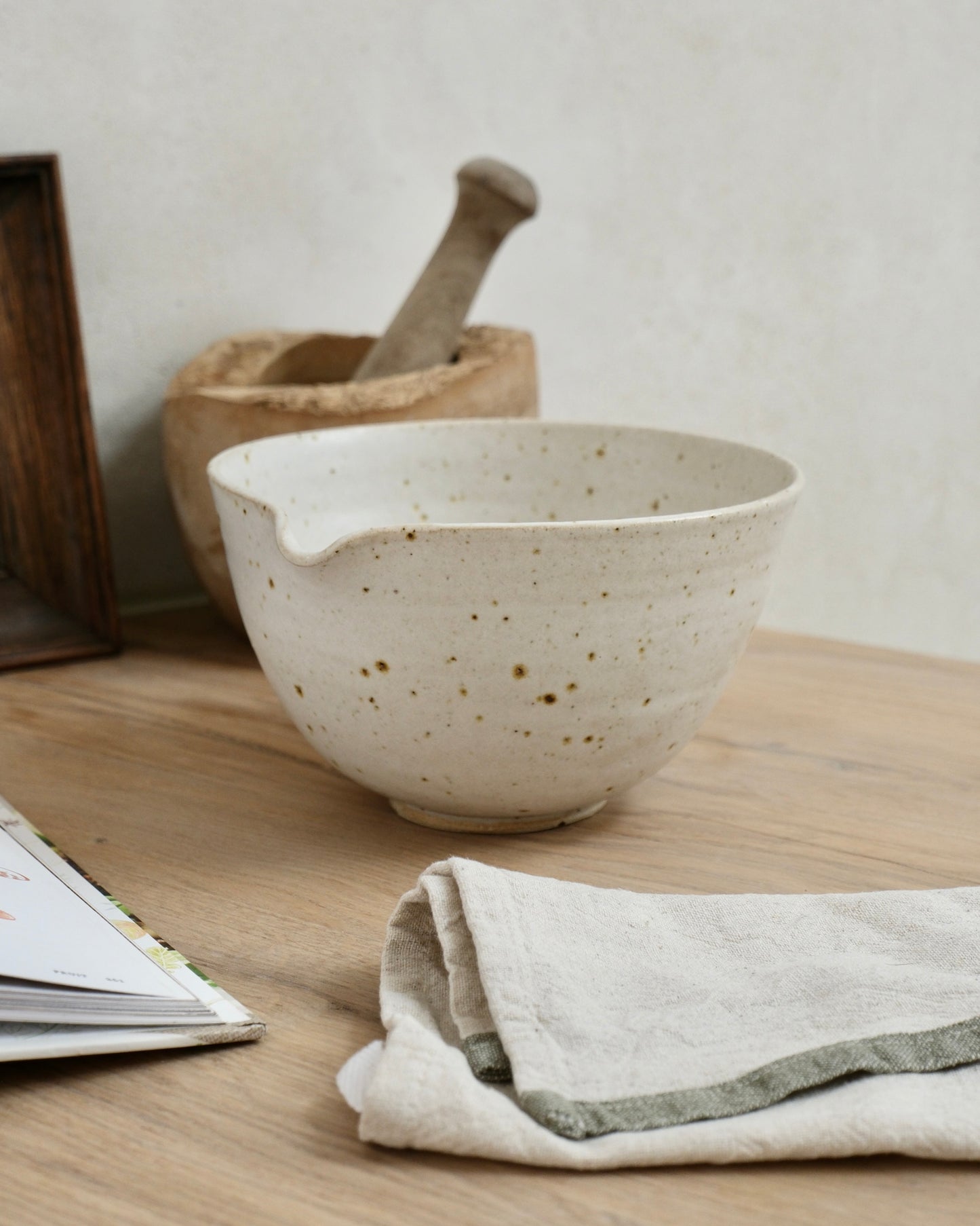 white Speckled ceramic mixing bowl on a wooden surface with a cloth and book in the background