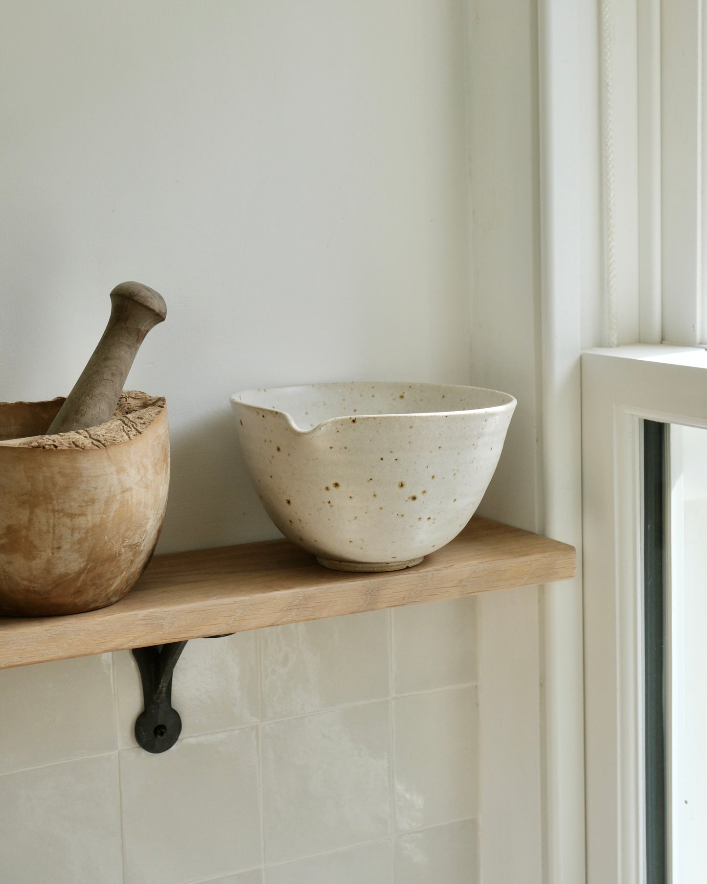 white ceramic mixing bowl on a wooden shelf against a light wall.