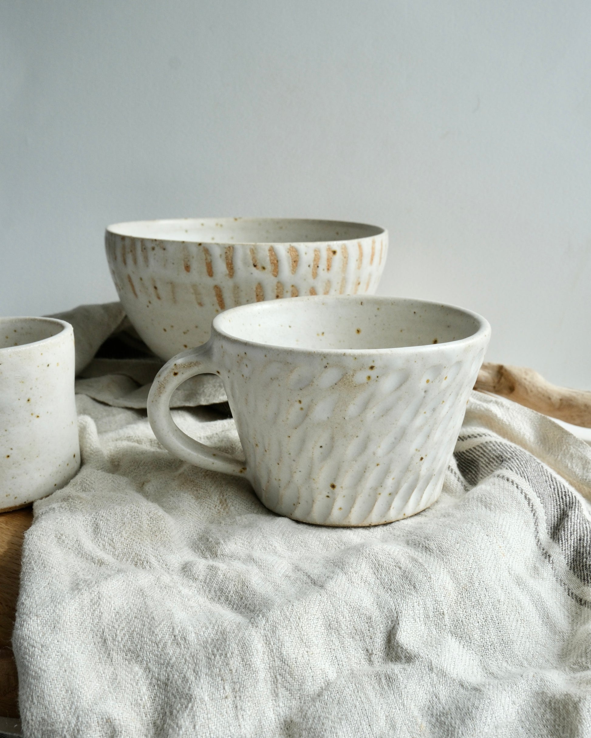 A collection of white stoneware pottery on a grey tea towel.