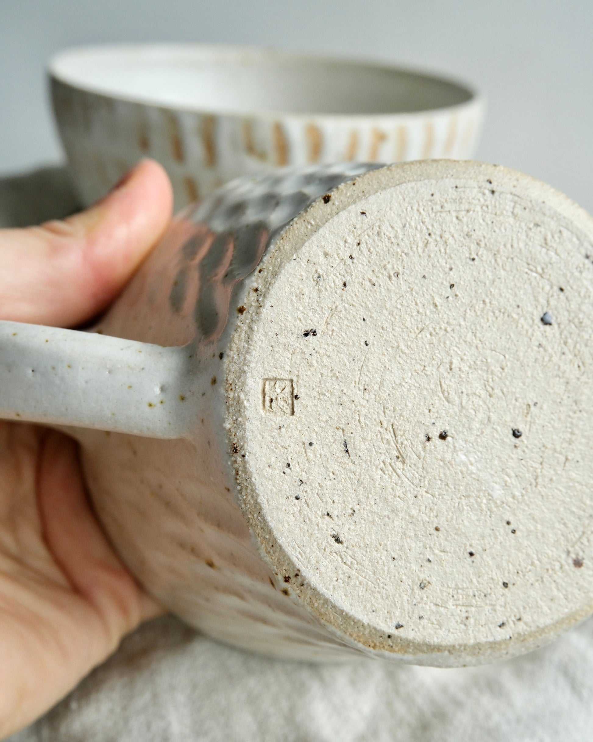 Close up of the bottom of a stoneware mug with a makers mark on the bottom