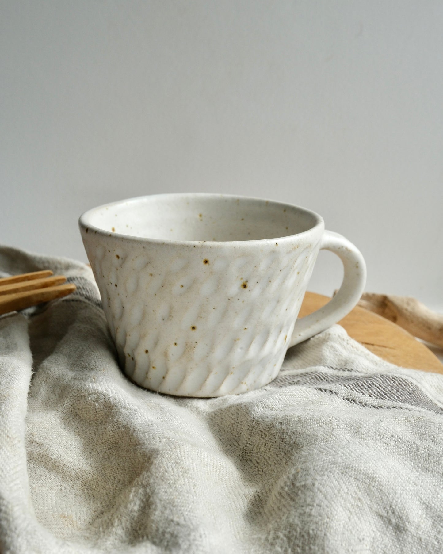 White textured ceramic coffee mug with a carved pattern on a tea towel