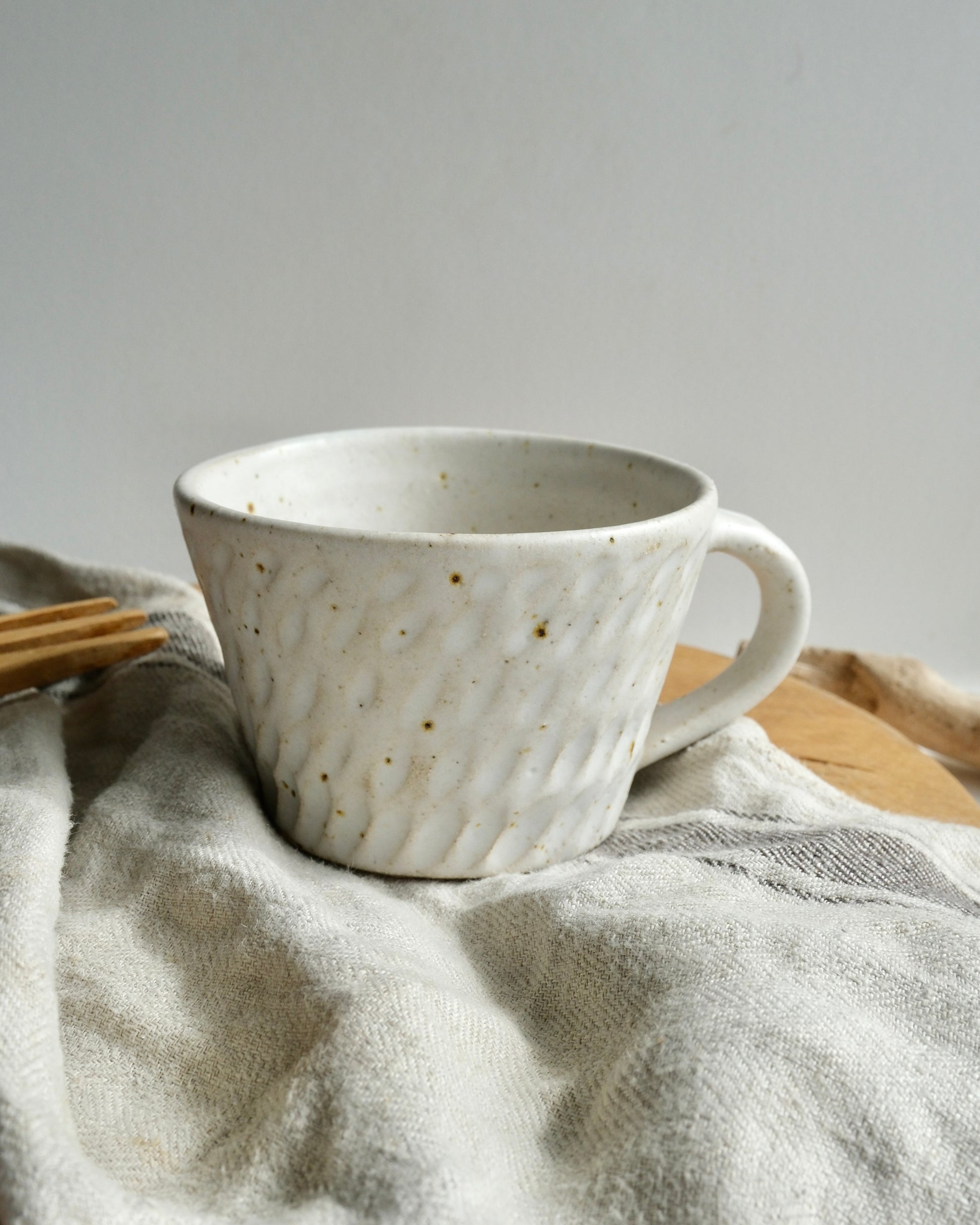 White textured ceramic coffee mug with a carved pattern on a tea towel