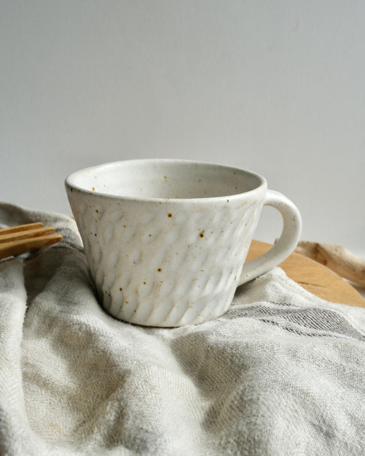 White textured ceramic coffee mug with a carved pattern on a tea towel