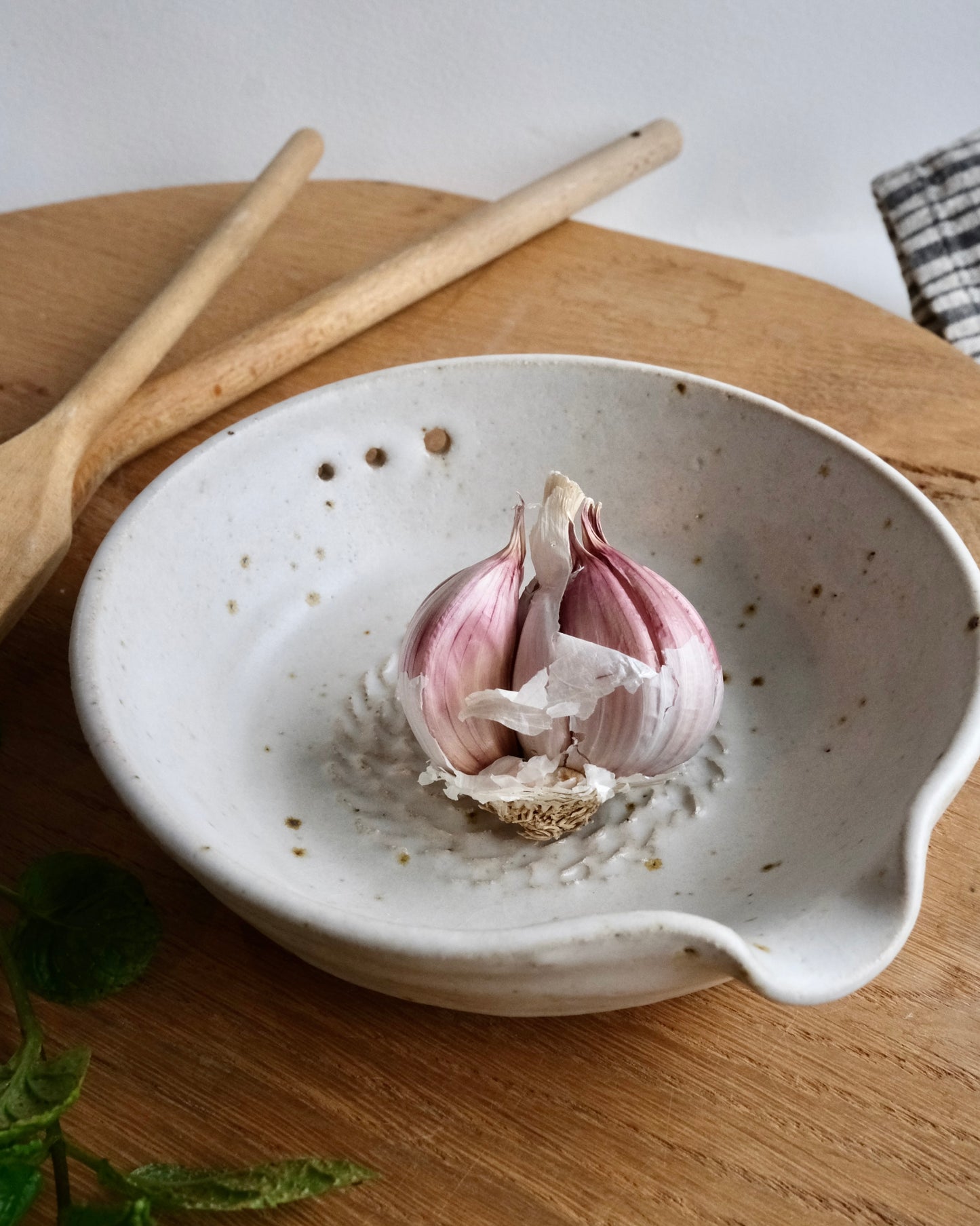 Garlic bulb in a handmade white ceramic bowl on a wooden surface