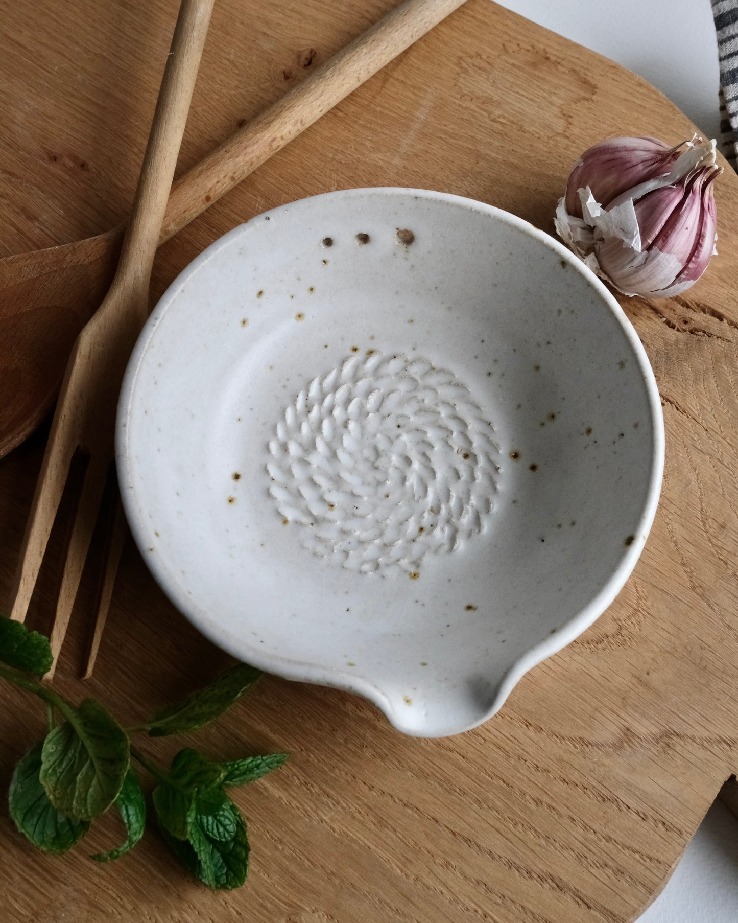 White ceramic dish with textured design on a wooden surface with garlic and mint leaves.