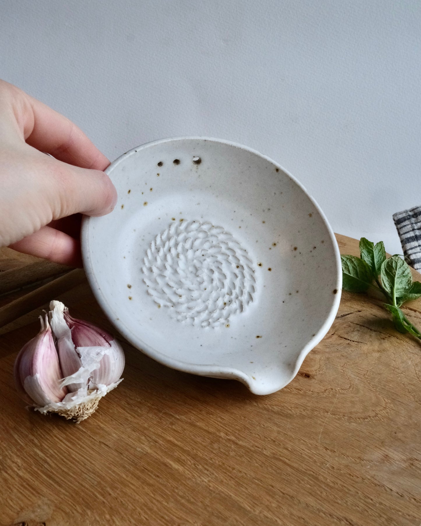Hand holding a white ceramic dish with a textured design on a wooden surface.