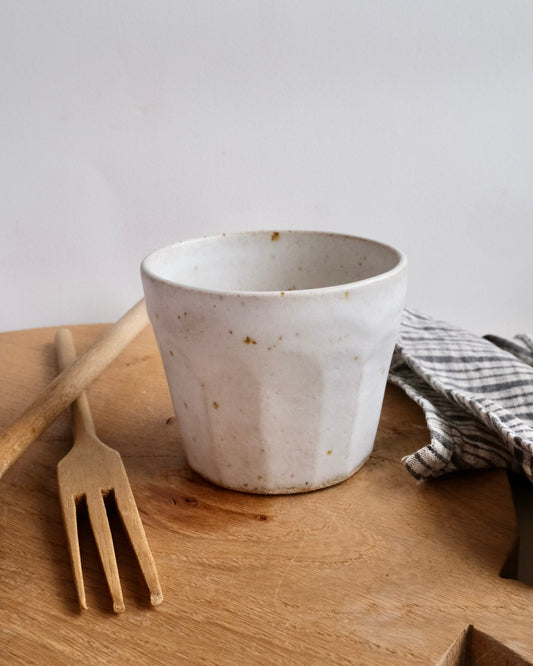 handmade White ceramic cup on a wooden surface with a fork and checkered cloth.