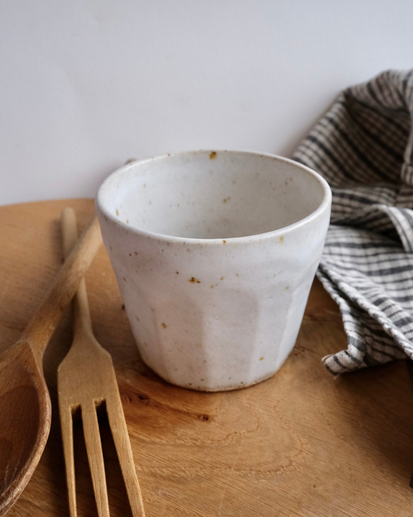 White ceramic cup on a wooden surface with a fork and striped towel in the background