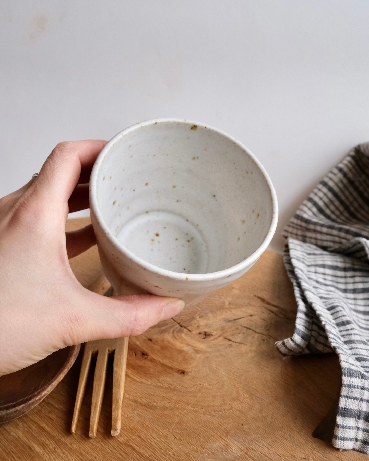 Hand holding a ceramic mug on a wooden surface with a striped towel in the background