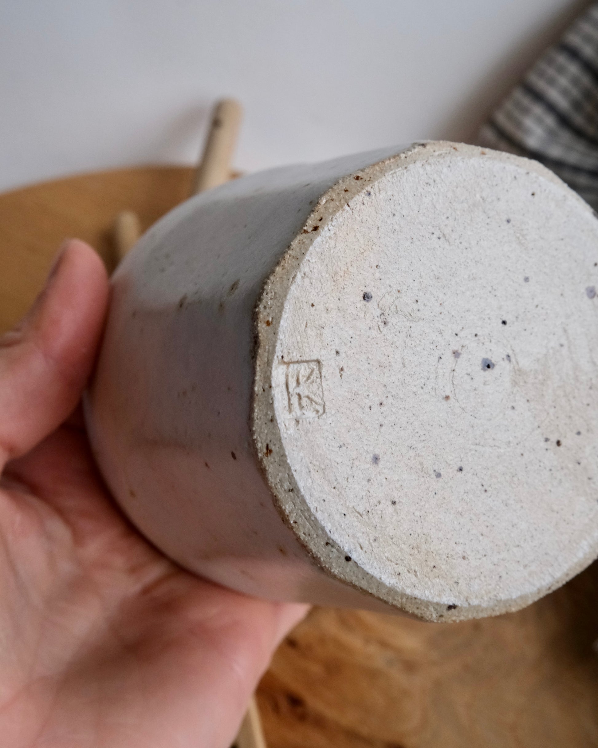 Hand holding a textured ceramic mug with a visible brand logo.