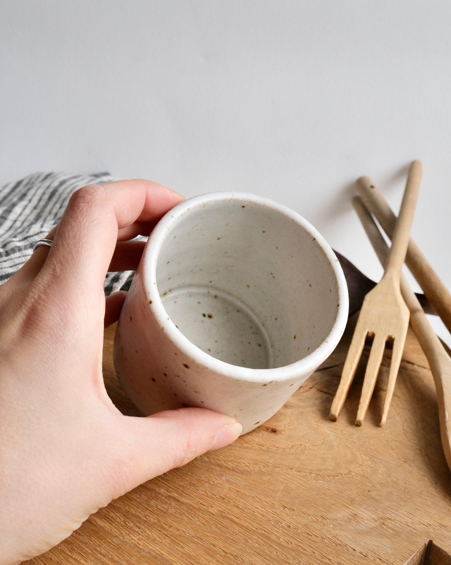 Hand holding a ceramic cup on a wooden surface with wooden utensils in the background