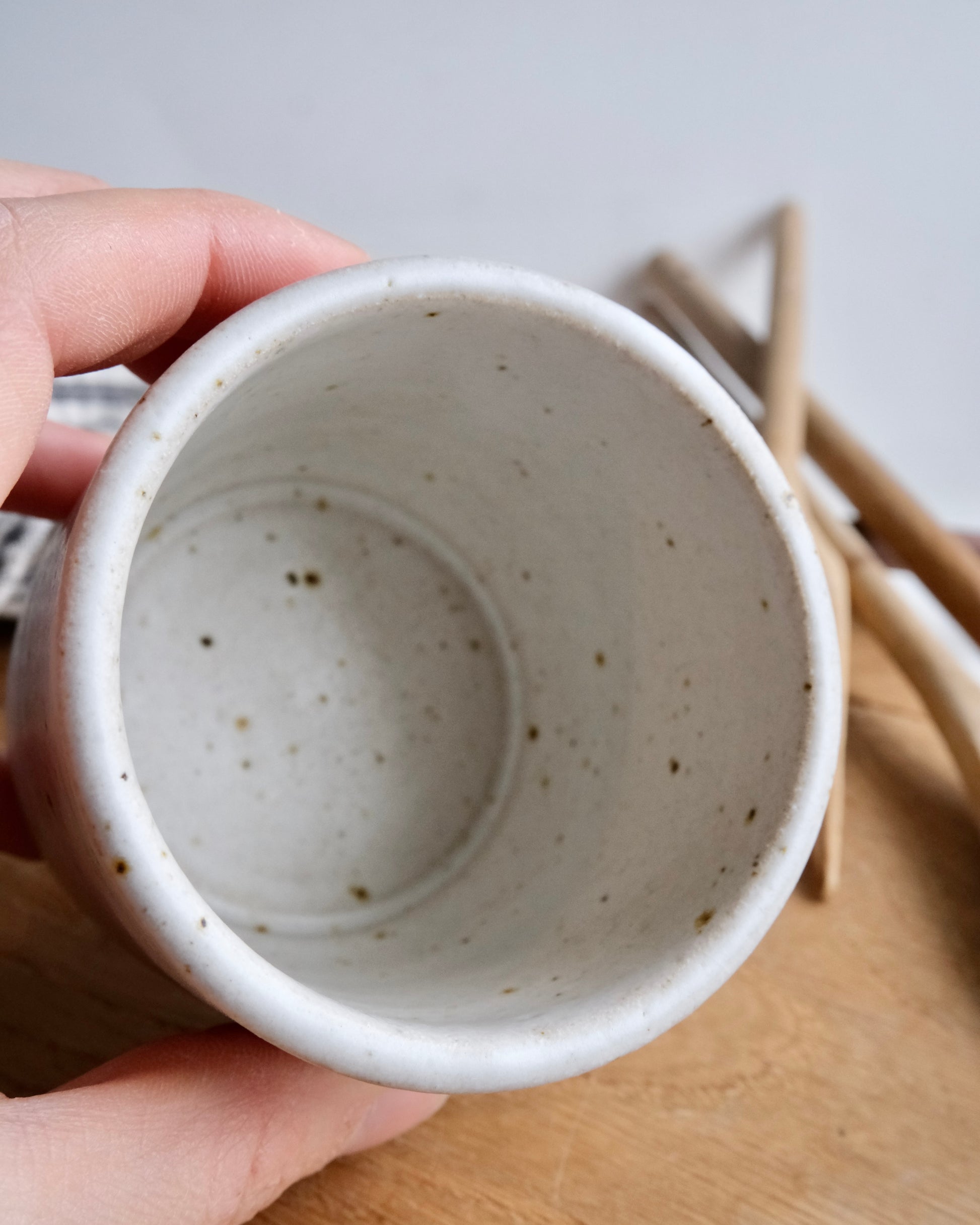 Hand holding a small ceramic cup with speckled texture on a wooden surface.
