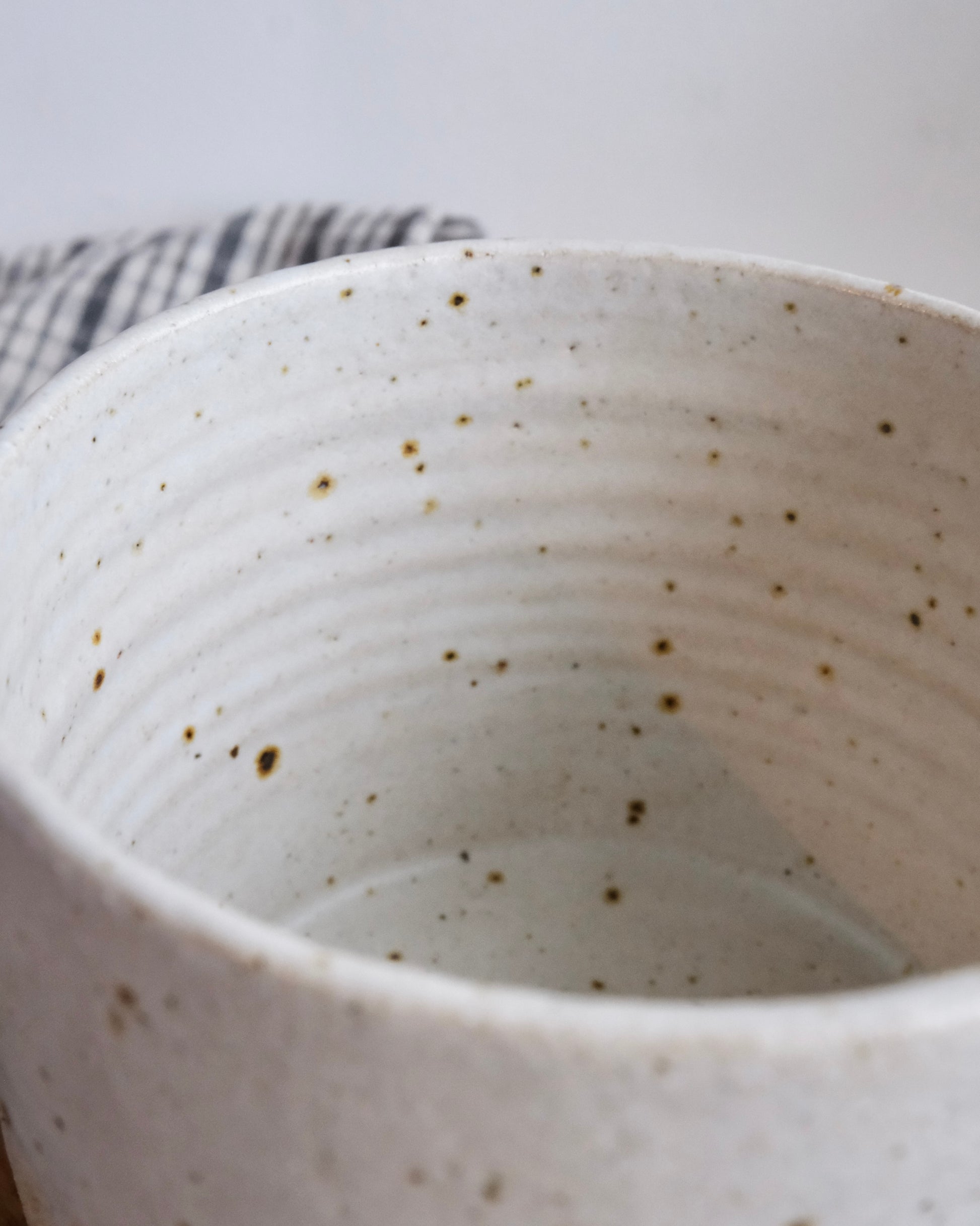 Close up of the speckled white glaze inside a medium ceramic pot.