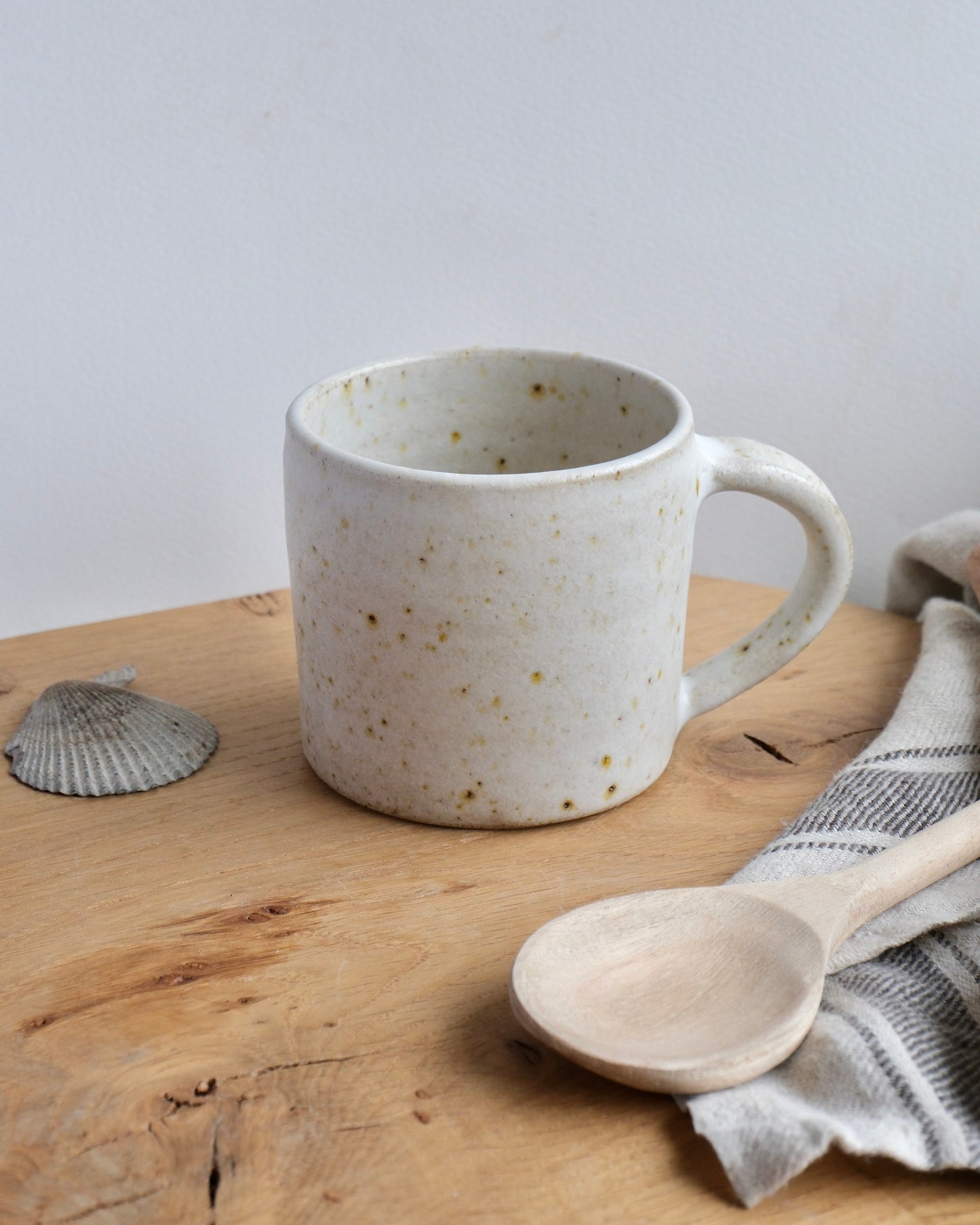 Speckled ceramic mug on a wooden surface with a wooden spoon and cloth.