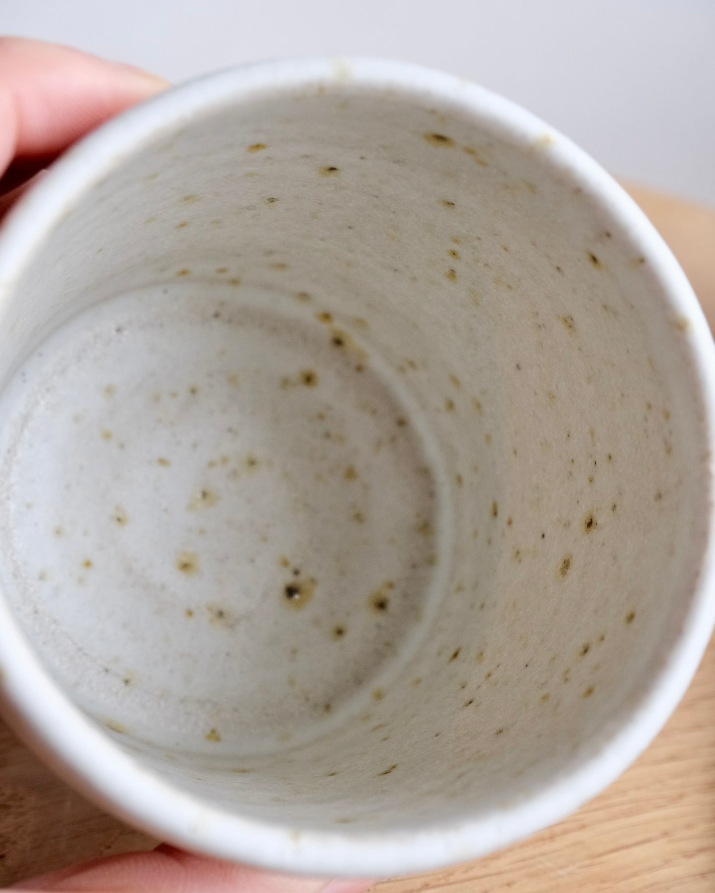 Close-up of a textured ceramic coffee mug held by a hand on a light background