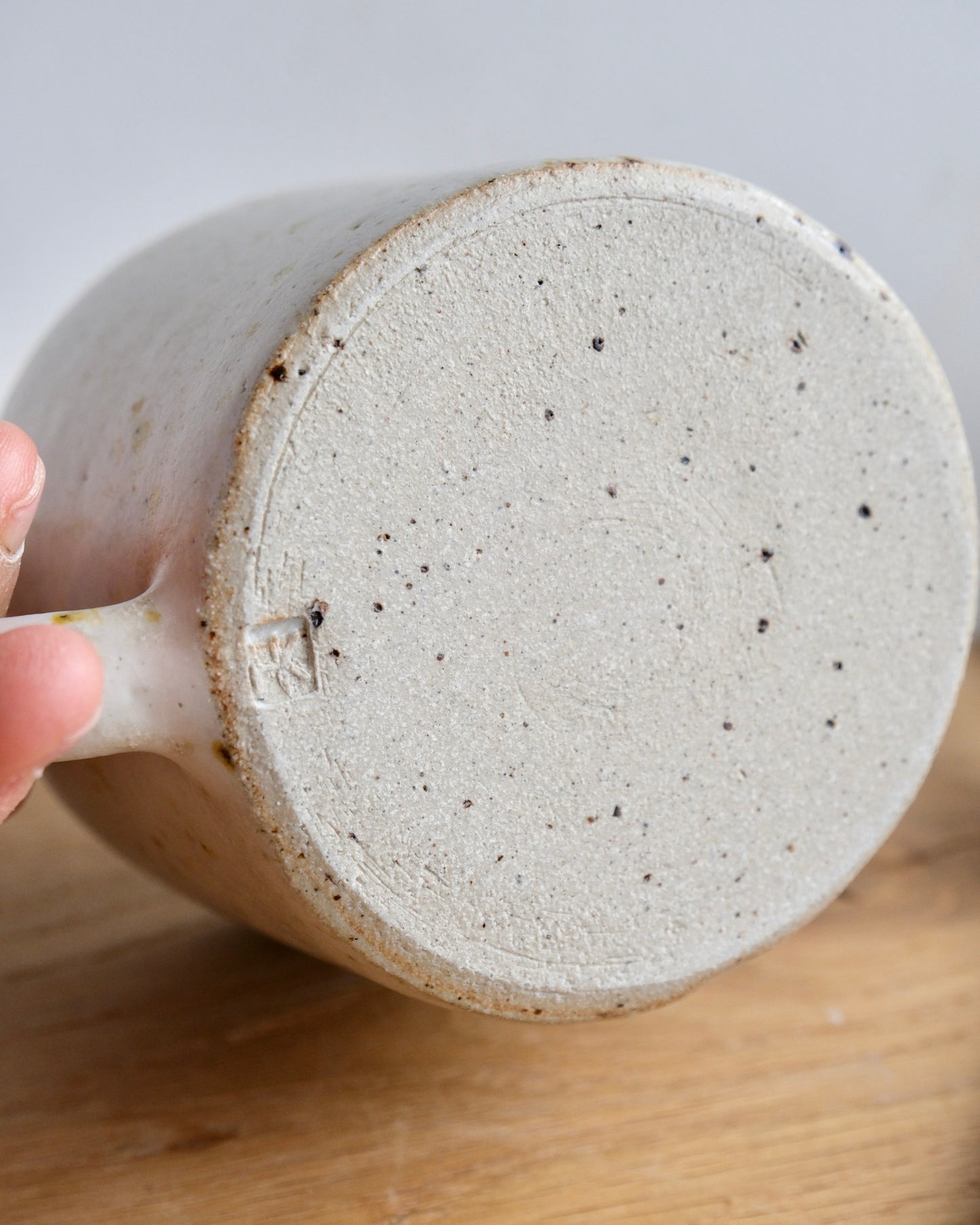 Close-up of a speckled ceramic mug held by a hand on a wooden surface.