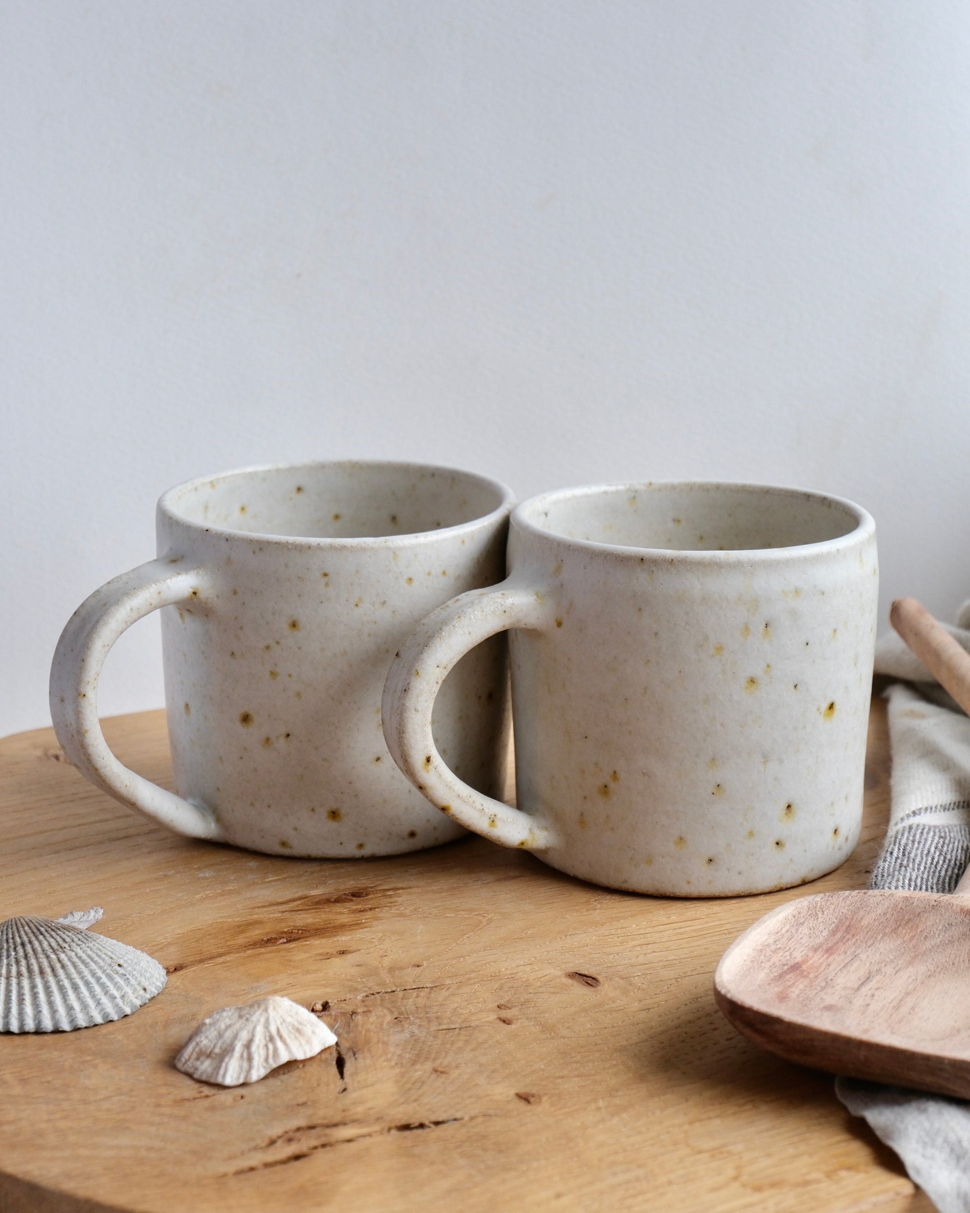 Two white speckled ceramic tea mugs on a wooden surface with a neutral background