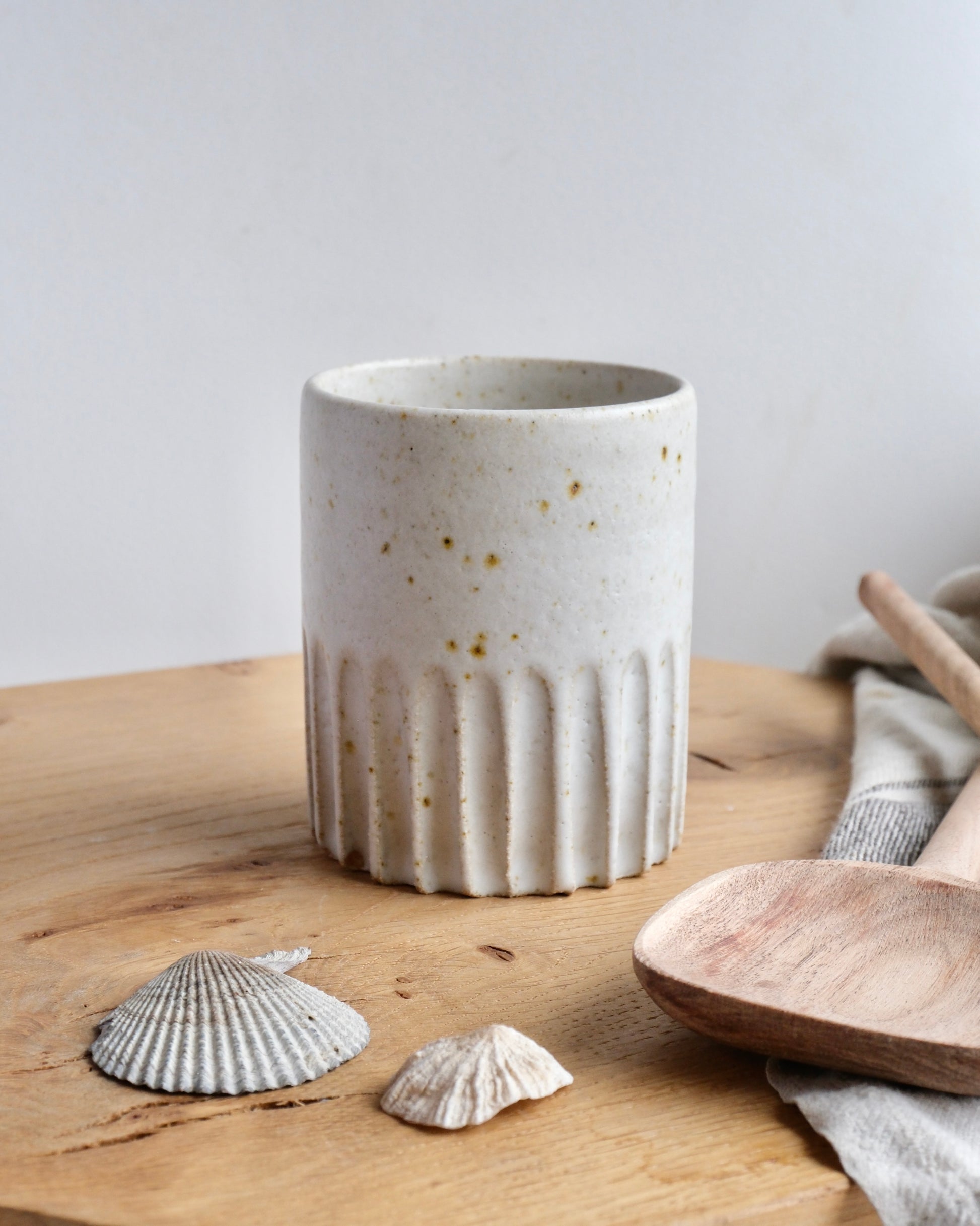 White ceramic cup with textured design on a wooden surface with shells and a wooden spoon.