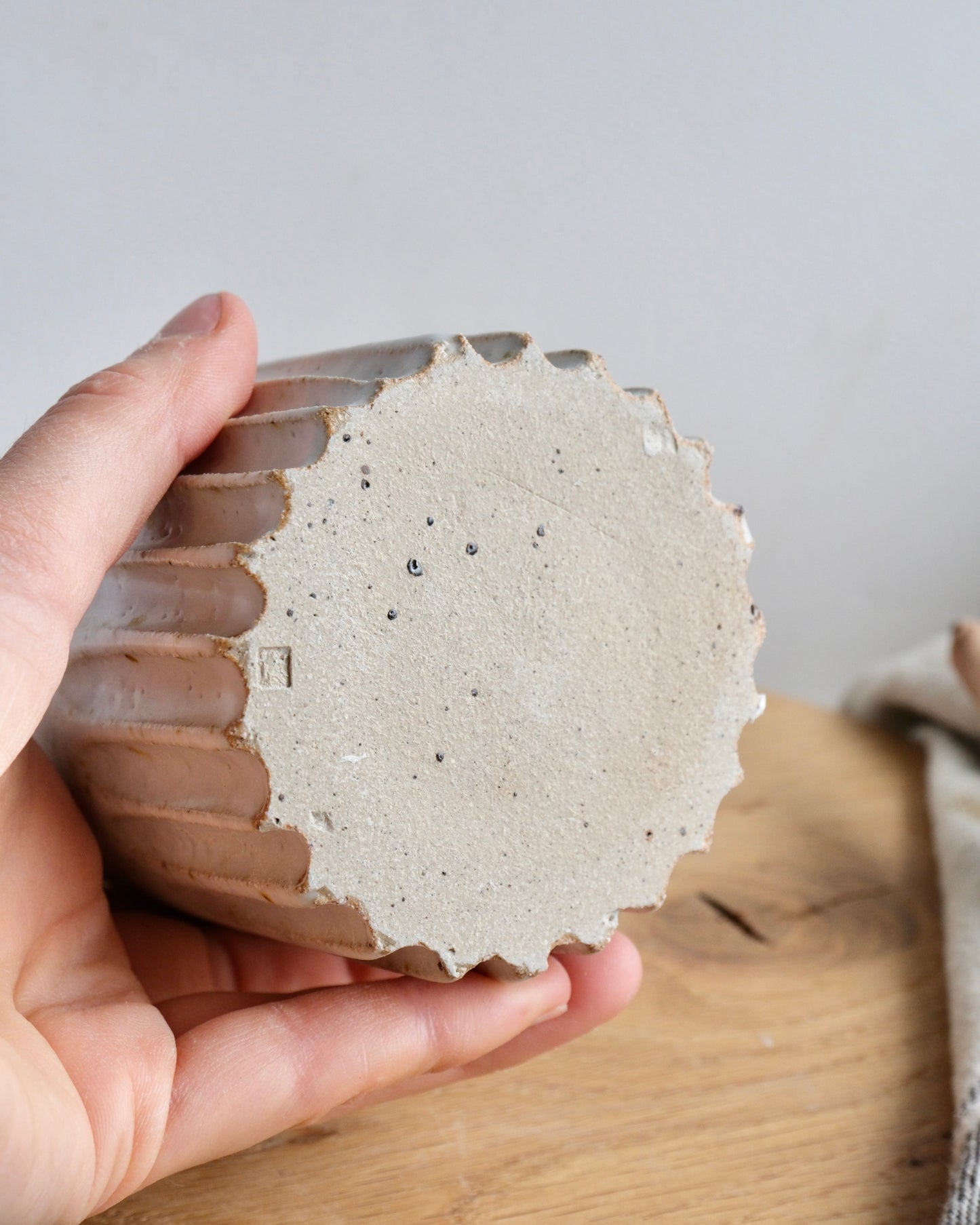 Hand holding a textured ceramic toothbrush holder on a wooden surface with a neutral background
