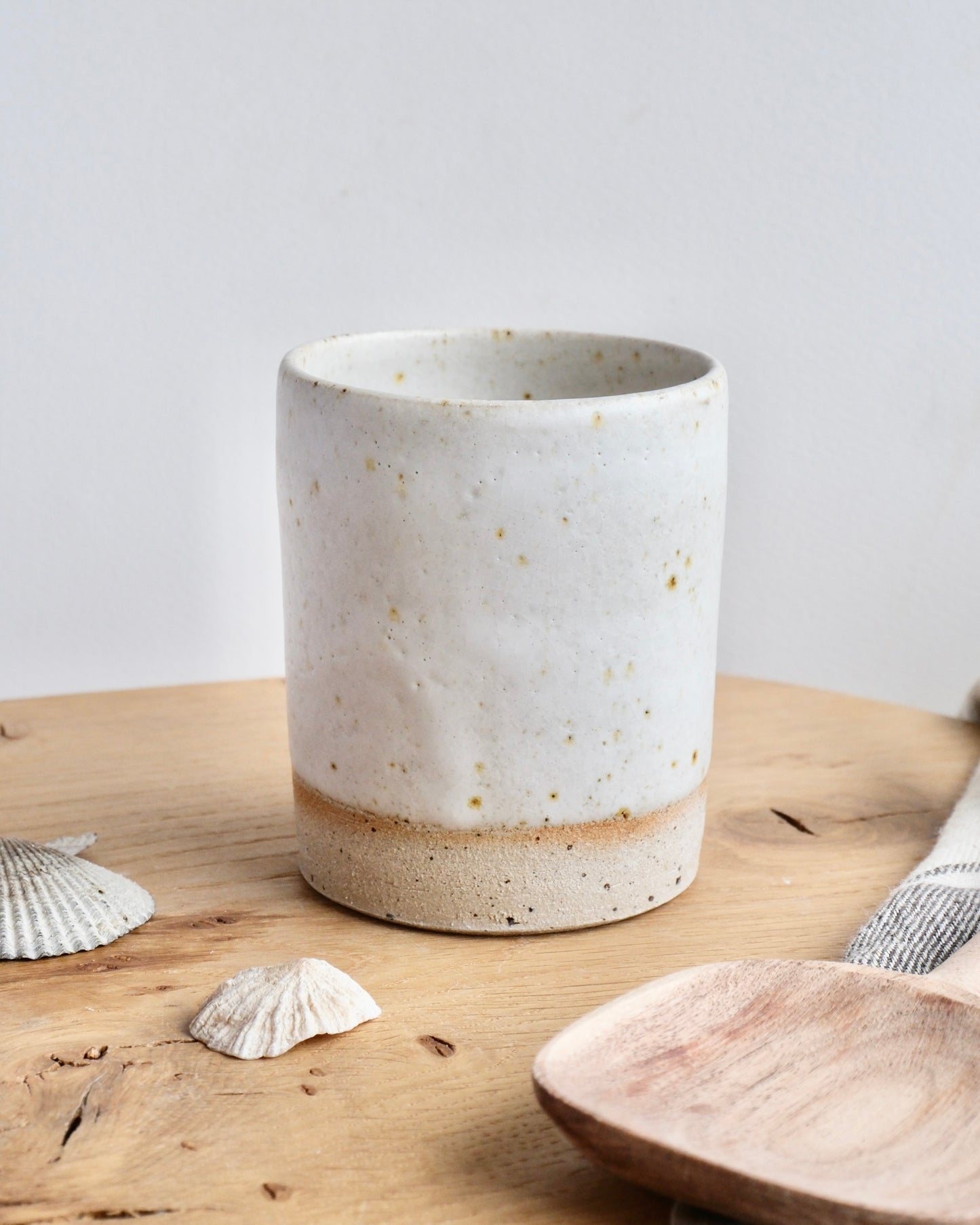A ceramic white speckled tall toothbrush pot on a wooden chopping board 