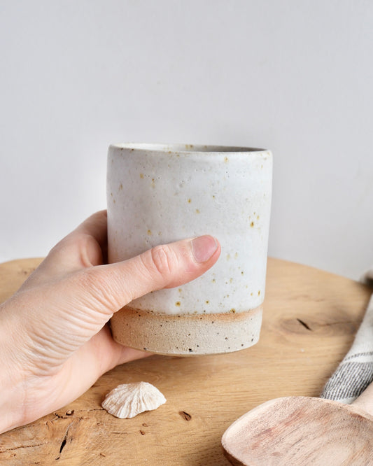 Hand holding a white ceramic pencil pot on a wooden surface with a light background