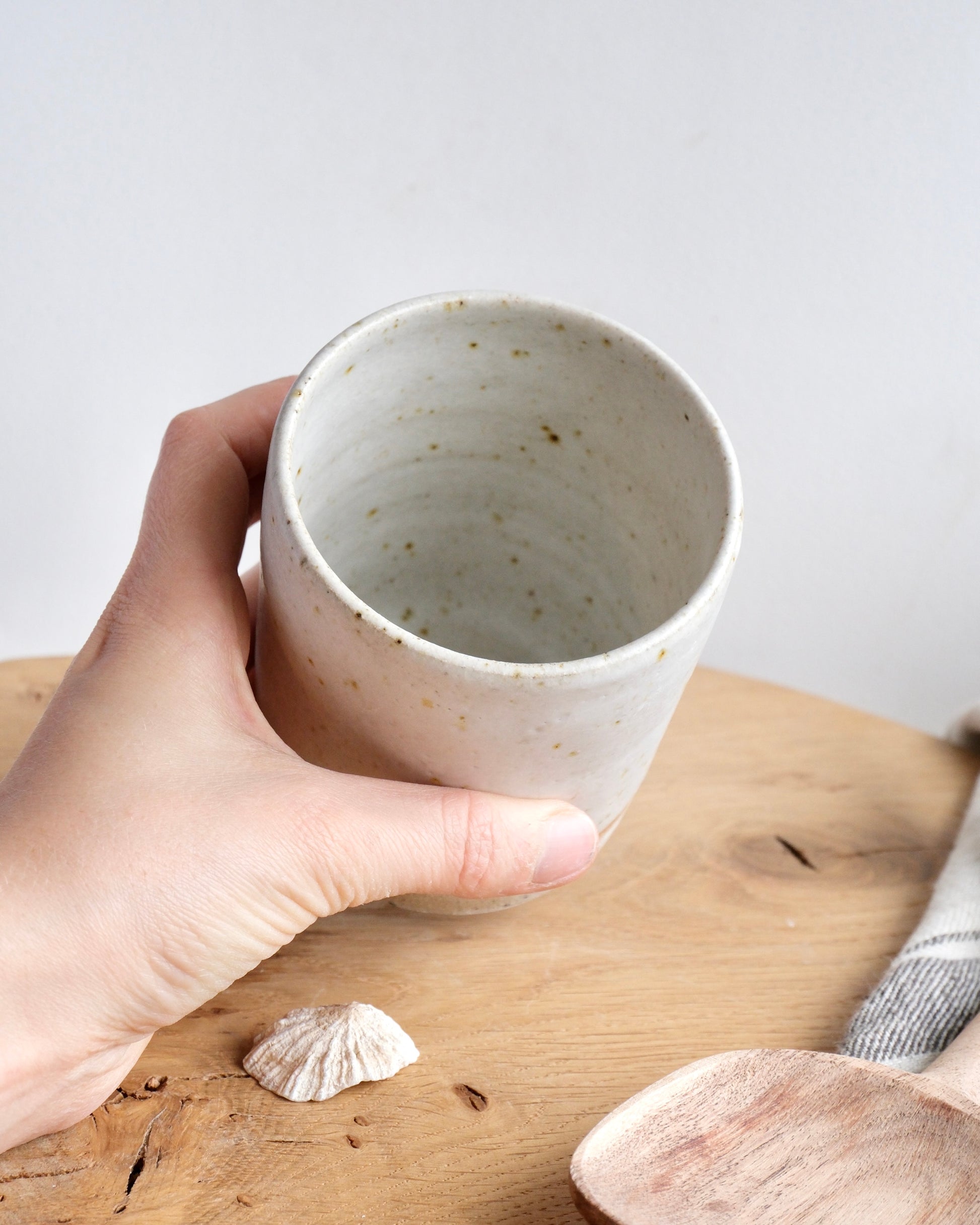 Hand holding a white speckled ceramic pencil pot on a wooden surface with a white background