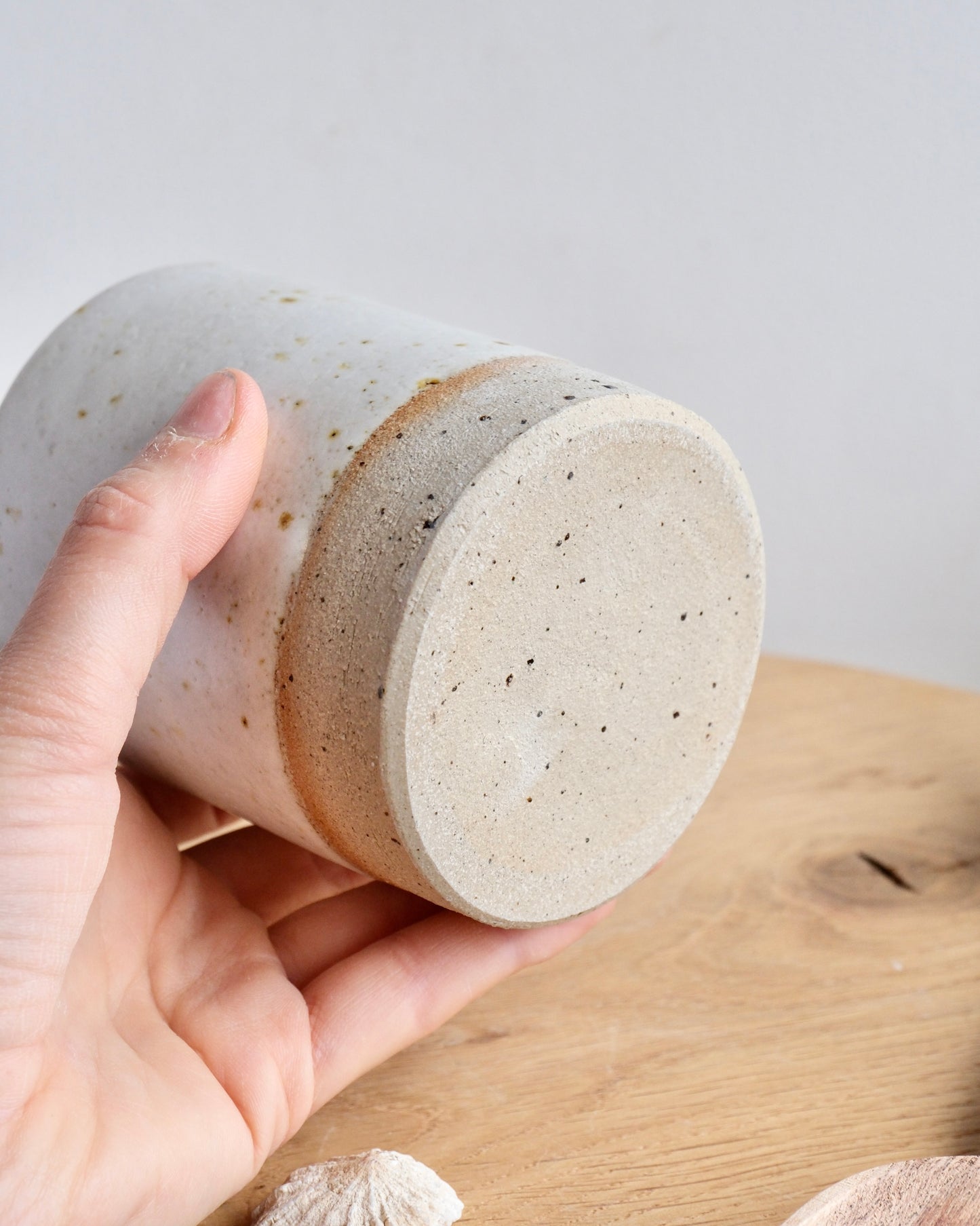Hand holding a textured ceramic cup on a wooden surface with a light gray background