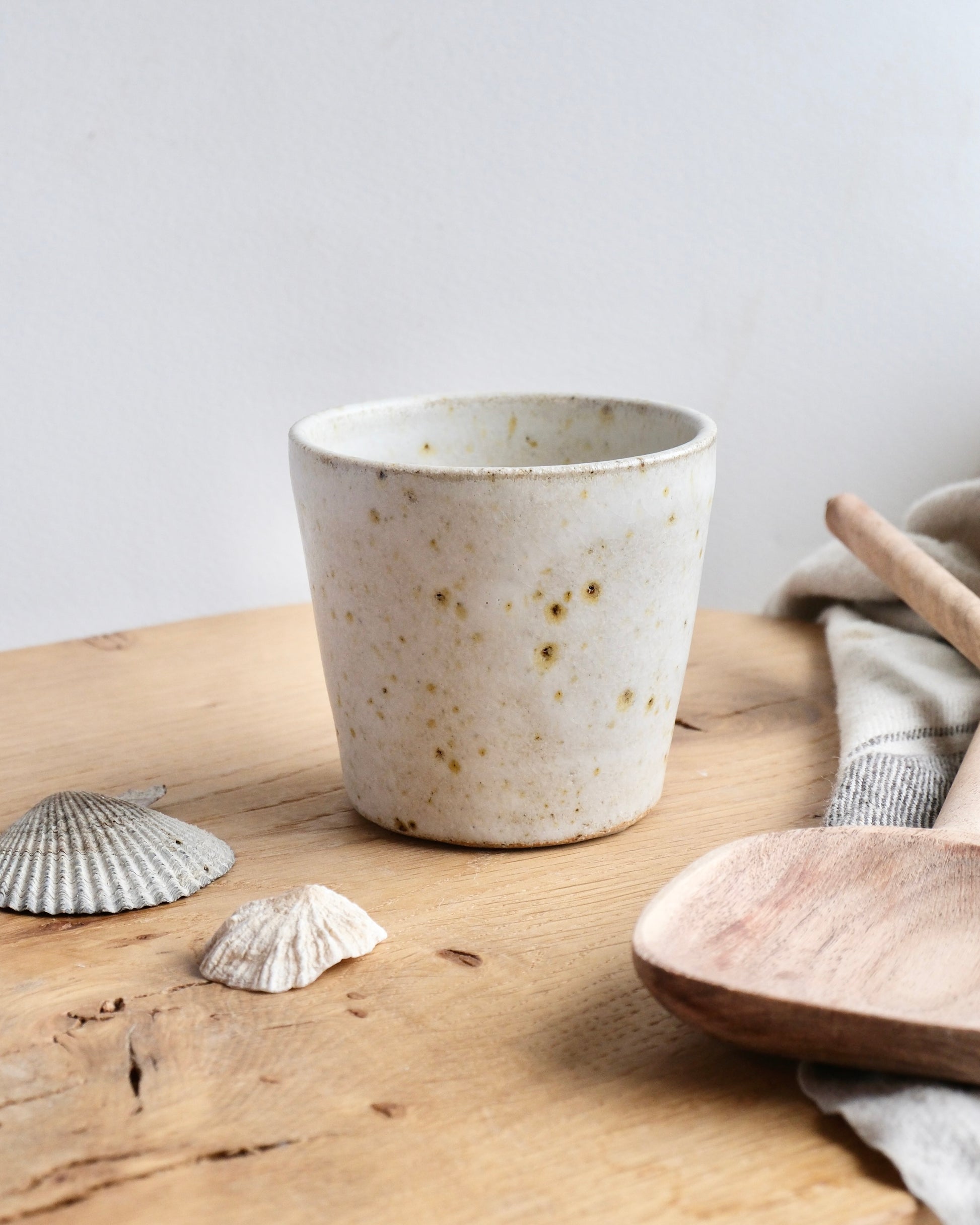 A white speckled stoneware cup on a wooden chopping board 