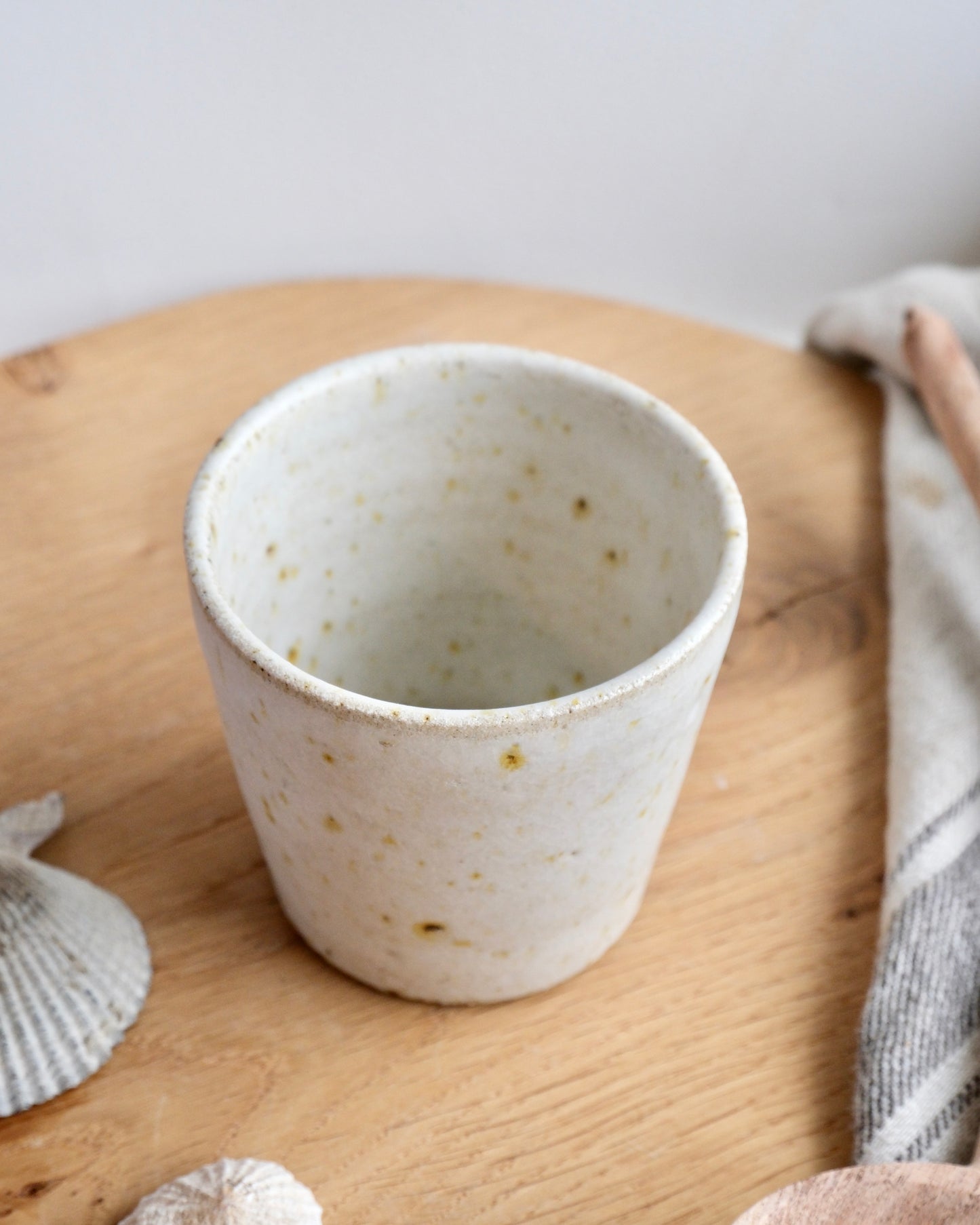 A white speckled stoneware cup on a wooden chopping board 
