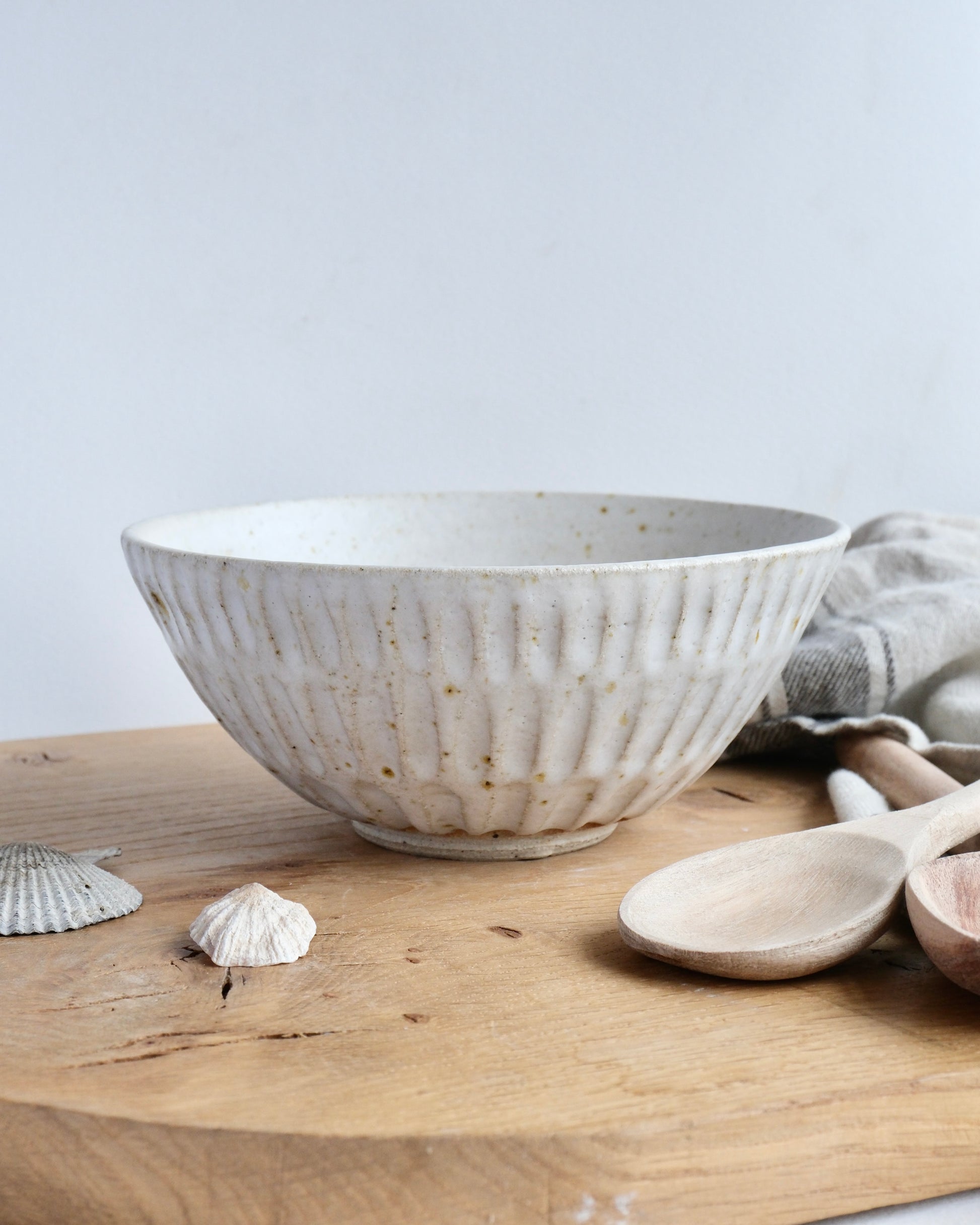 Handmade white stoneware breakfast bowl with a textured carved design on a wooden chopping board