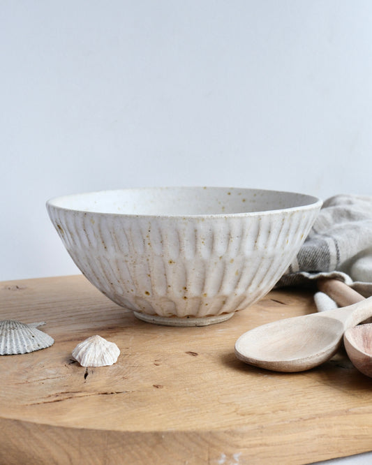 Handmade white stoneware breakfast bowl with a textured carved design on a wooden chopping board